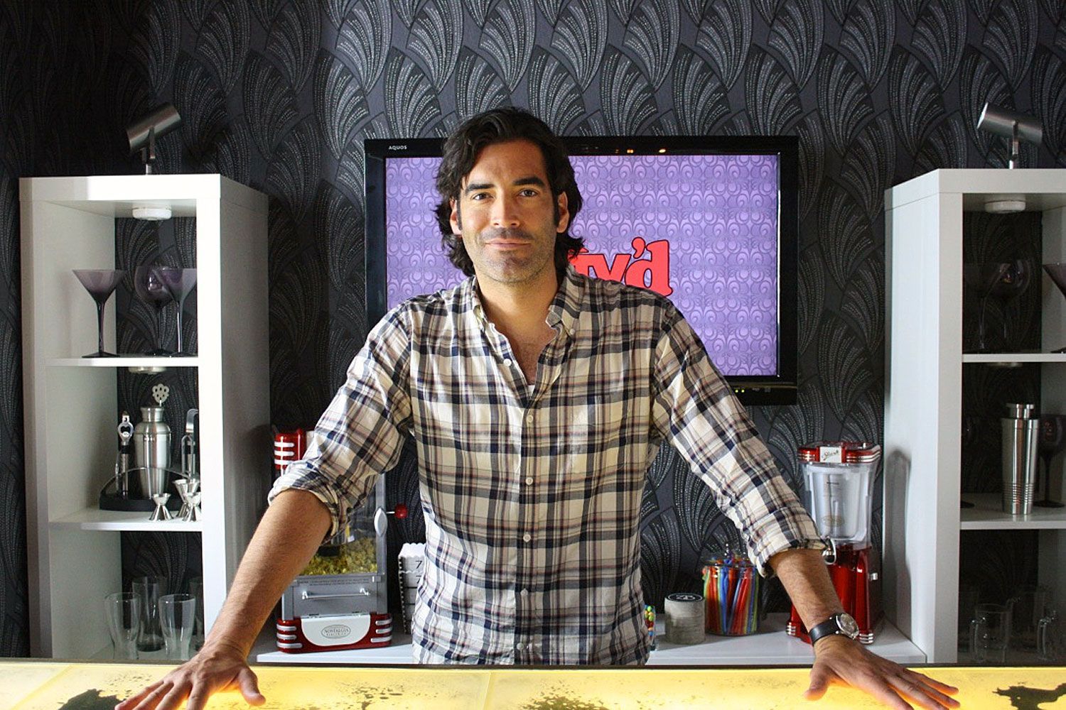 HGTV host  in a plaid shirt is standing in front of a tv leaning on a liquid lave countertop