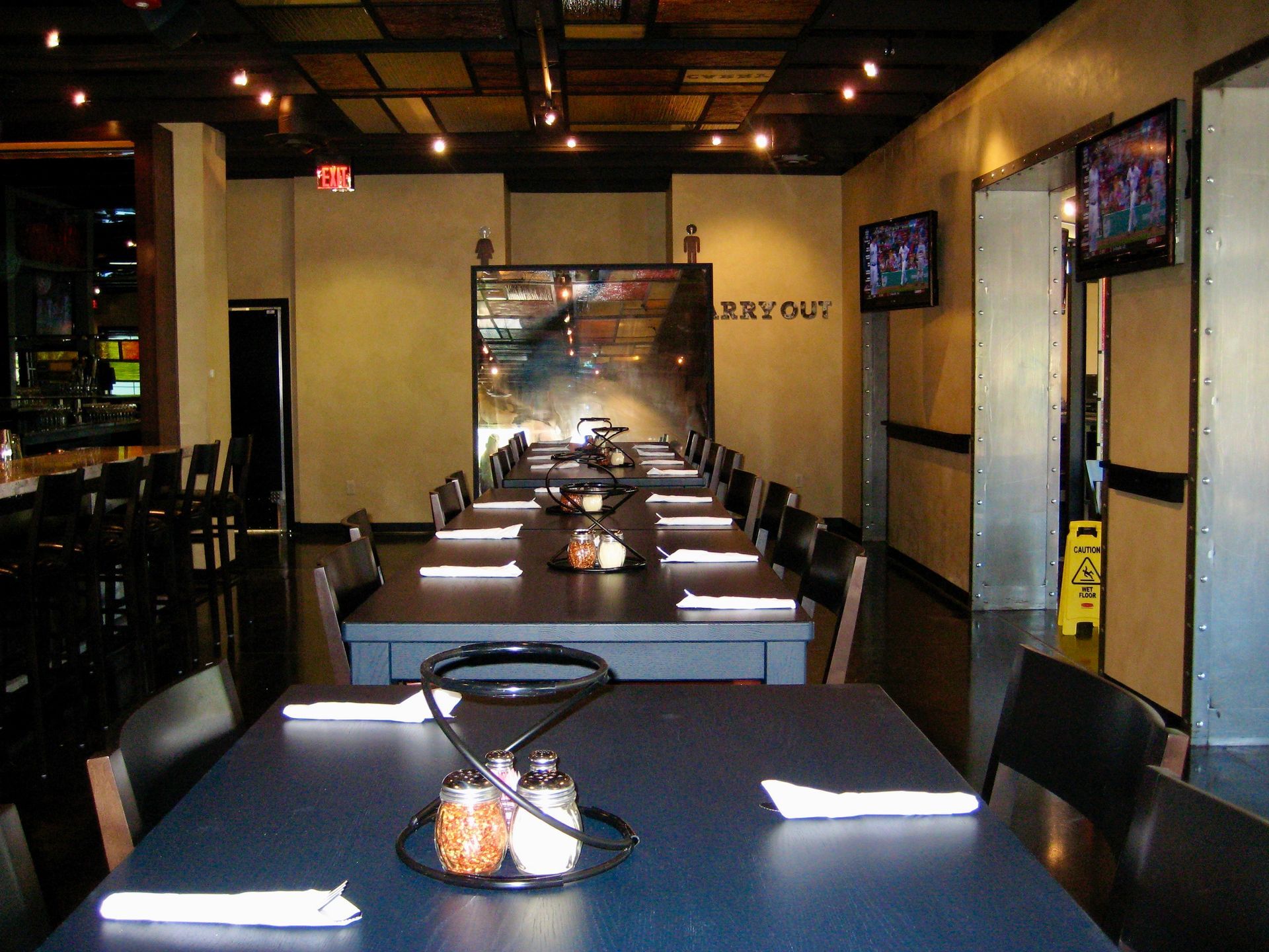 Empty restaurant dining area with dark tables, chairs, and warm lighting, viewed down a central aisle