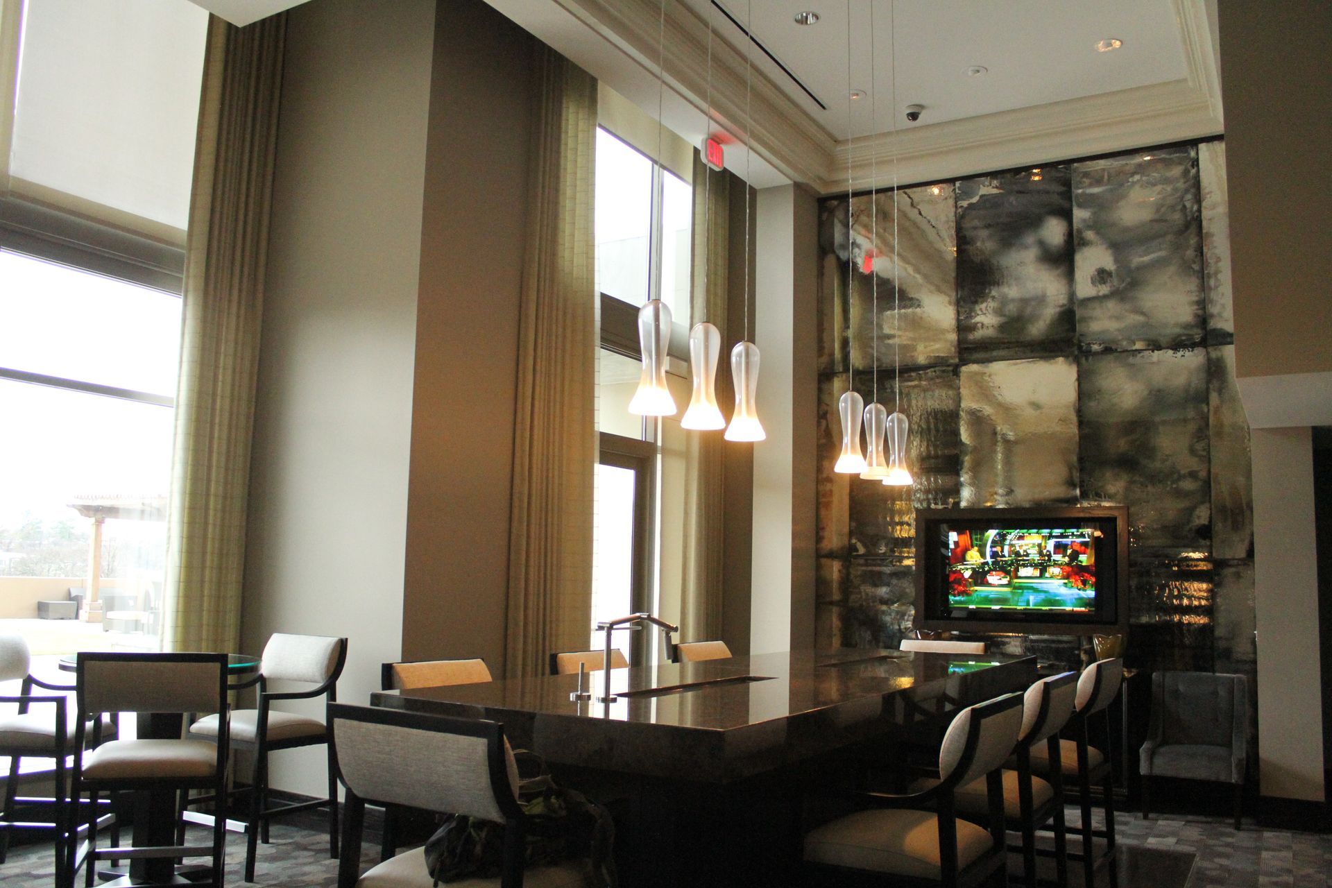 Modern lounge with bar, chairs, large windows, and decorative mirror wall, featuring a TV.