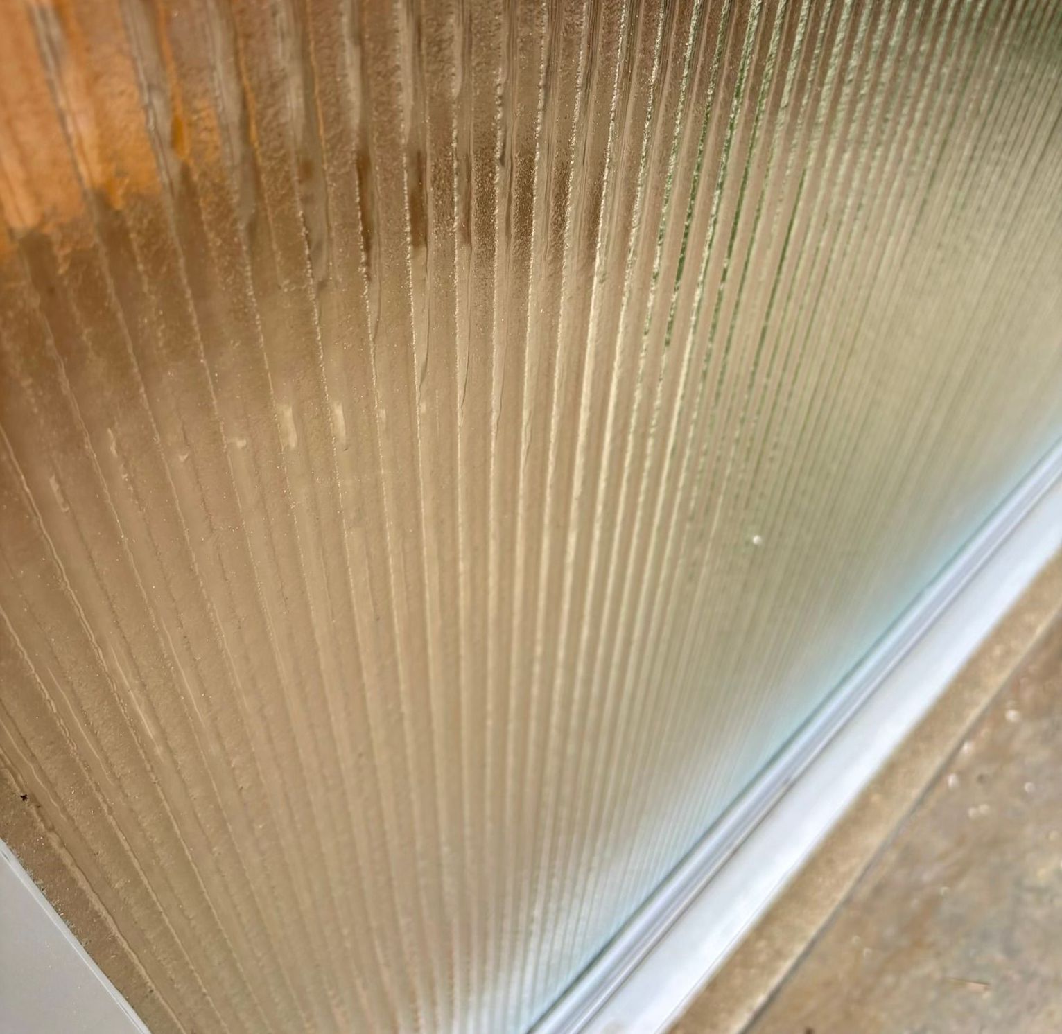 Textured glass door, with vertical ribbed pattern, next to white frame and concrete.