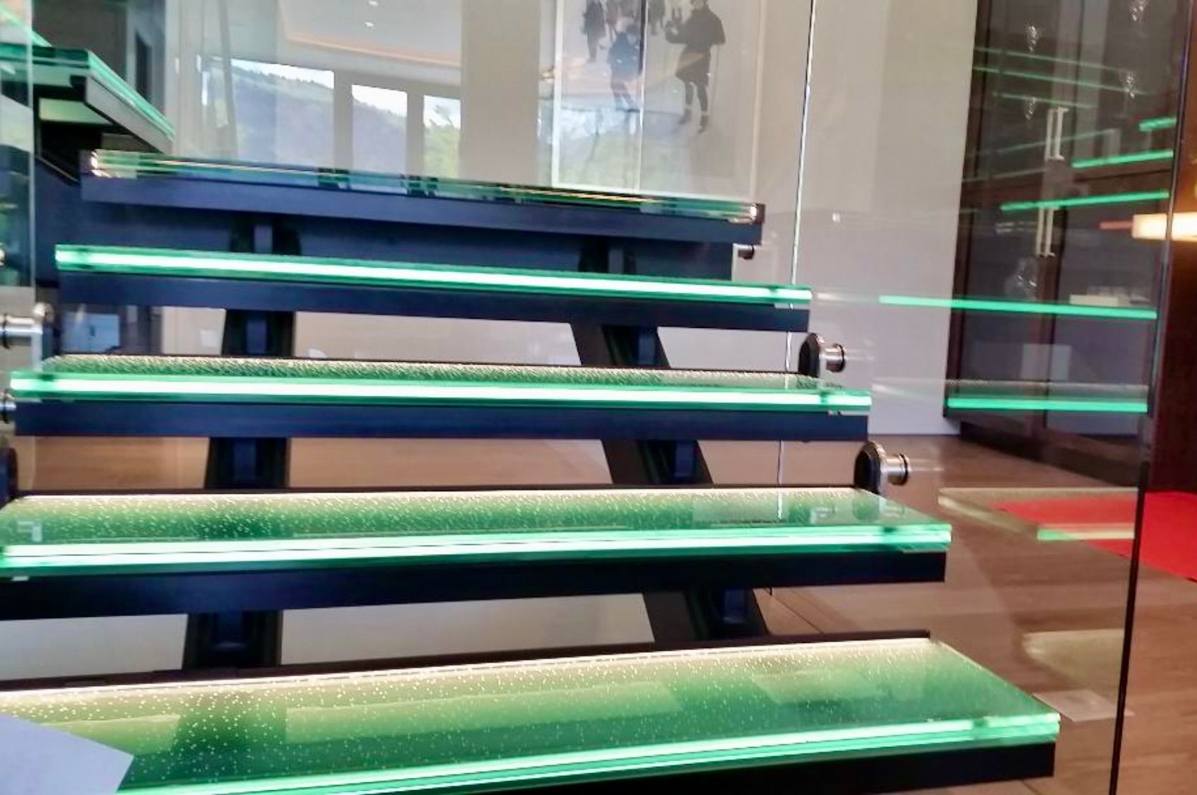 Modern staircase with illuminated green glass steps and a glass railing.
