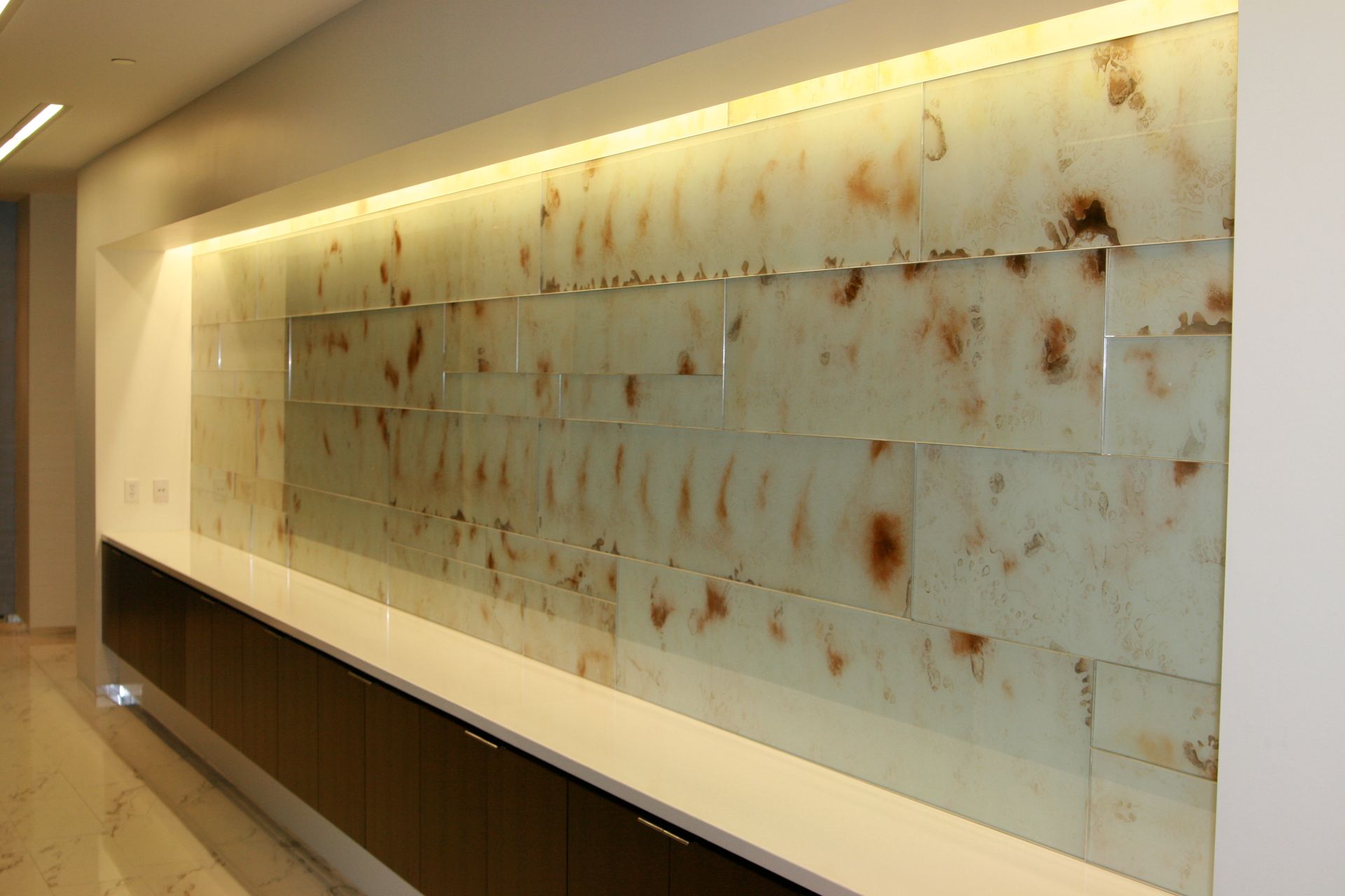 Wall with brown and white textured panels, white counter, and brown cabinets below.