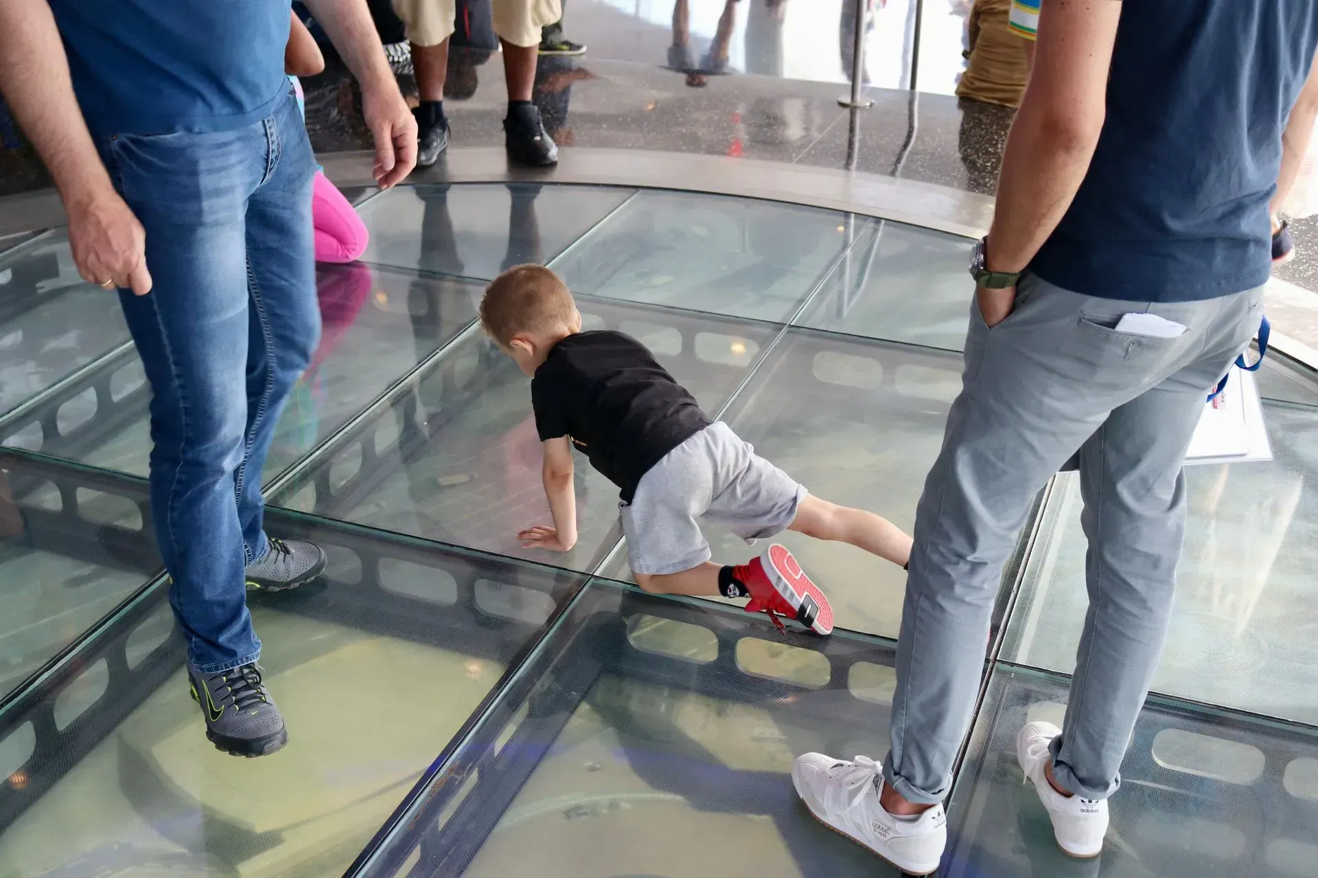 A little boy is crawling on a glass floor in a museum.