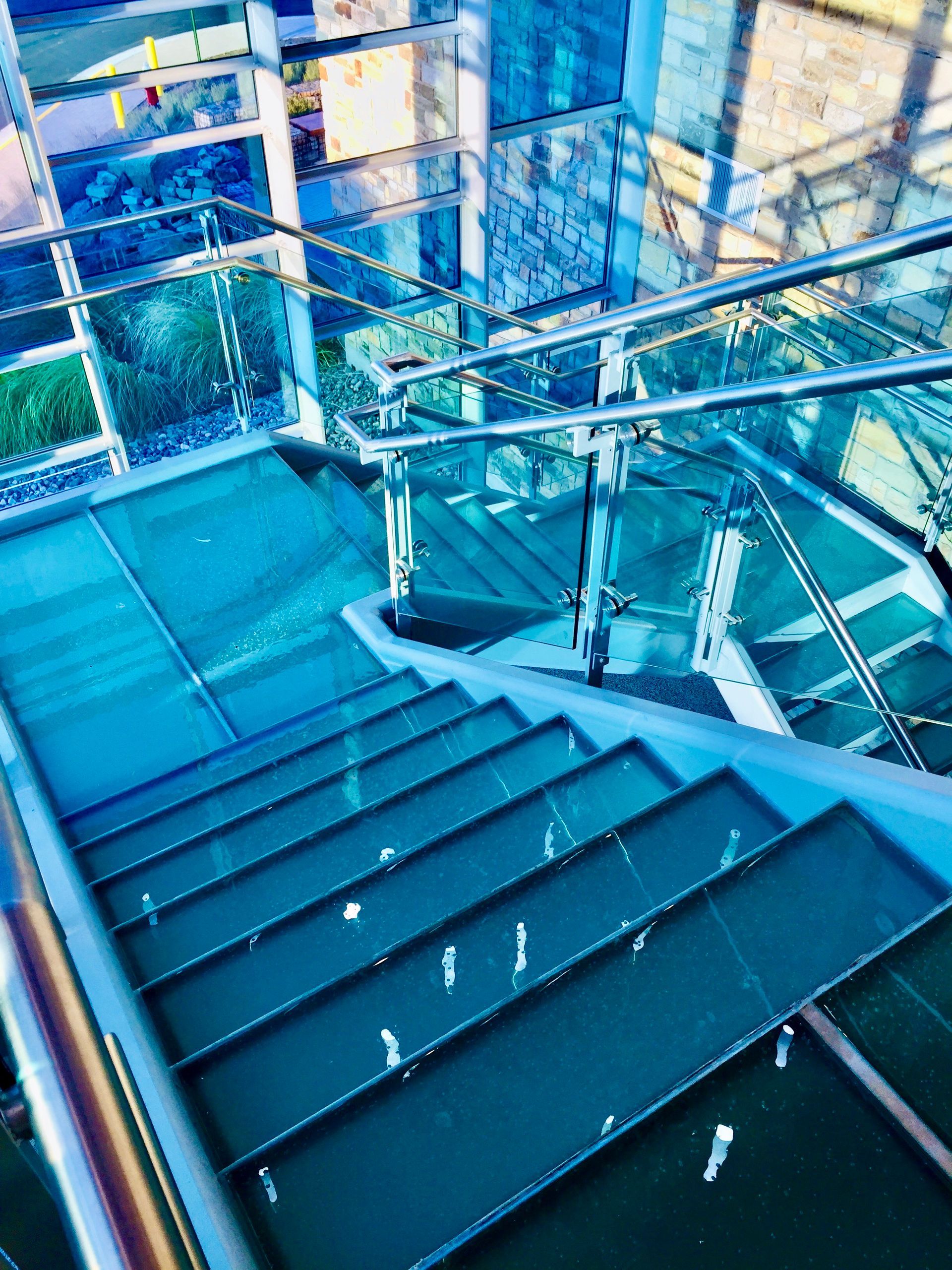 Glass staircase with blue tint, descending from a modern building's upper level.