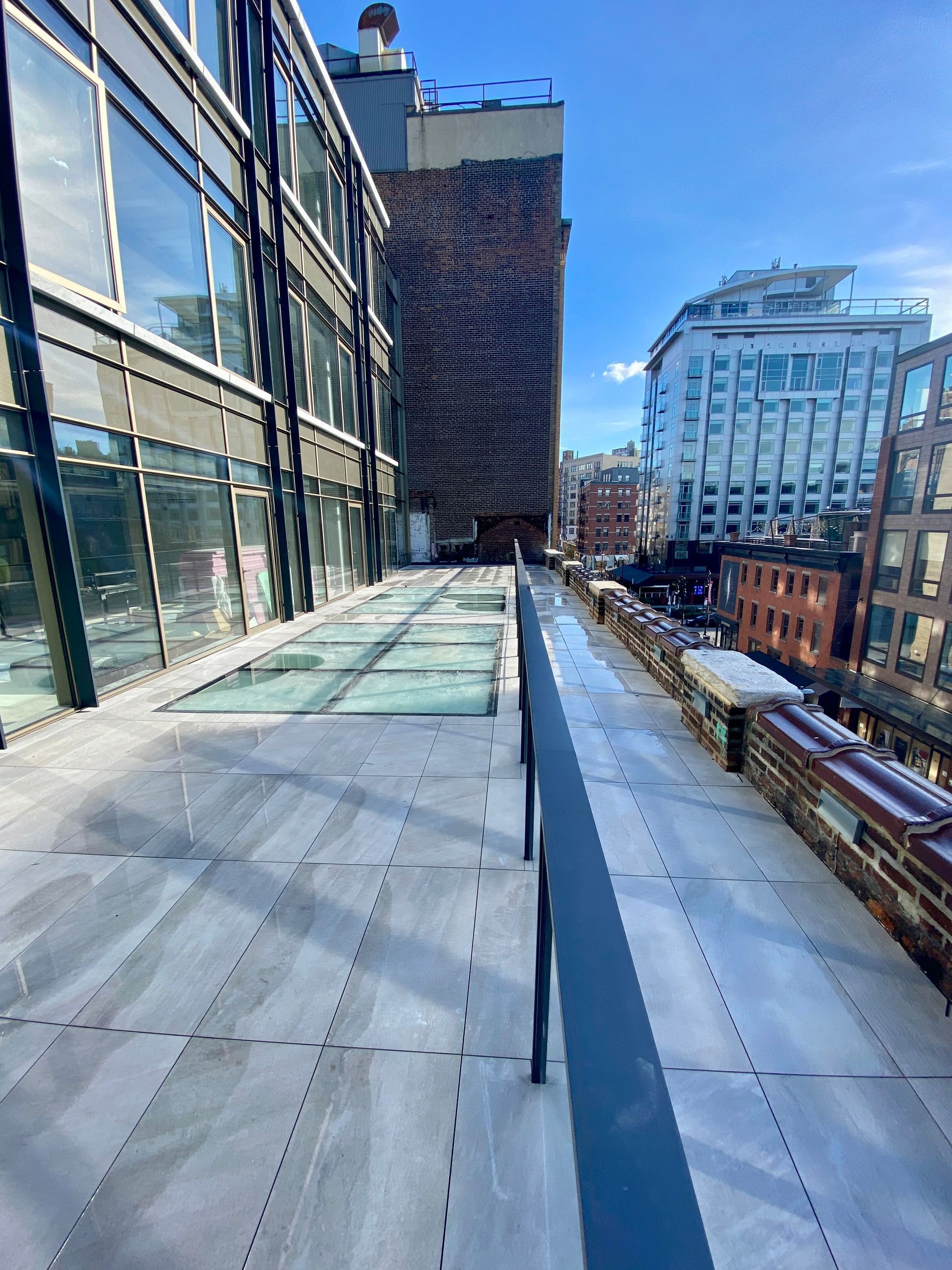 A rooftop terrace with light-colored pavers, a glass floor skylight