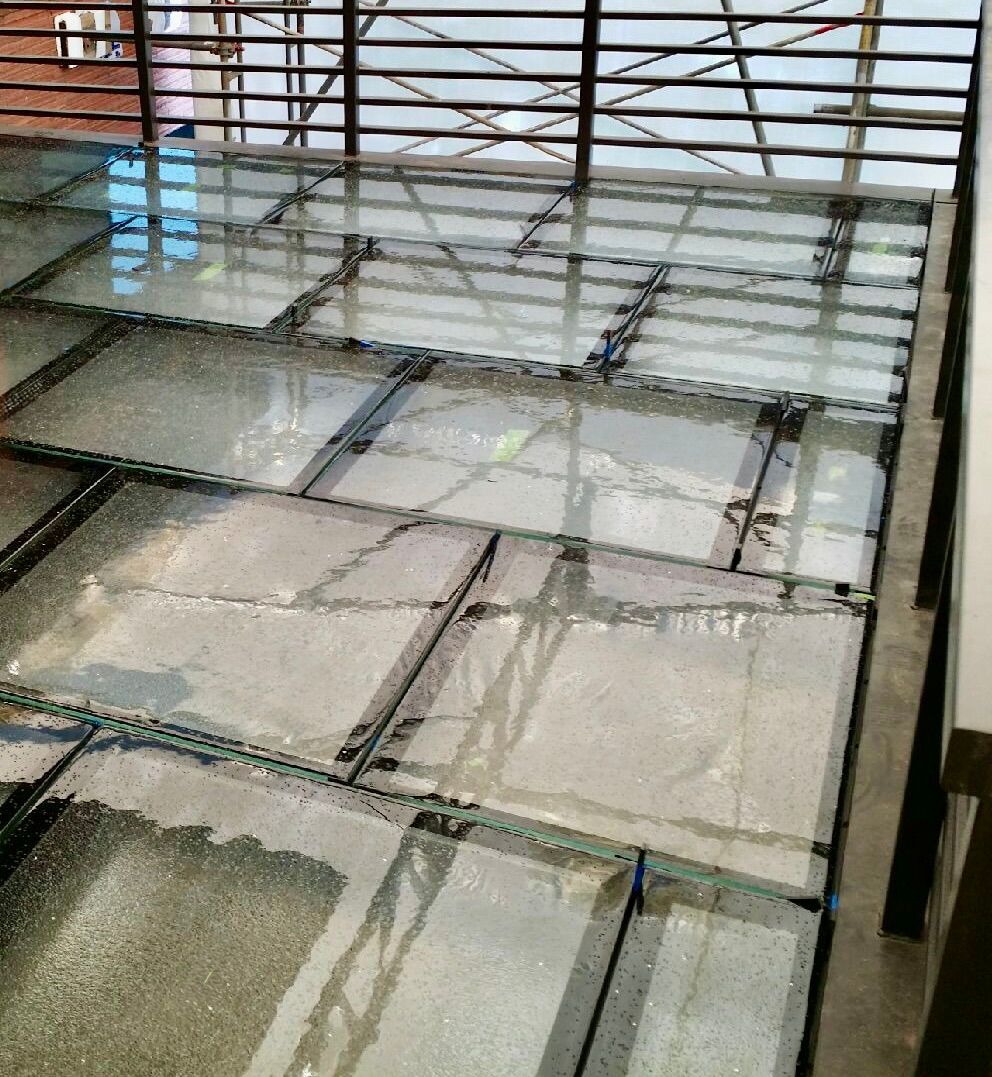 A high-angle view of a tiled floor surface with a reflective, semi-transparent glass panel installed in the center.