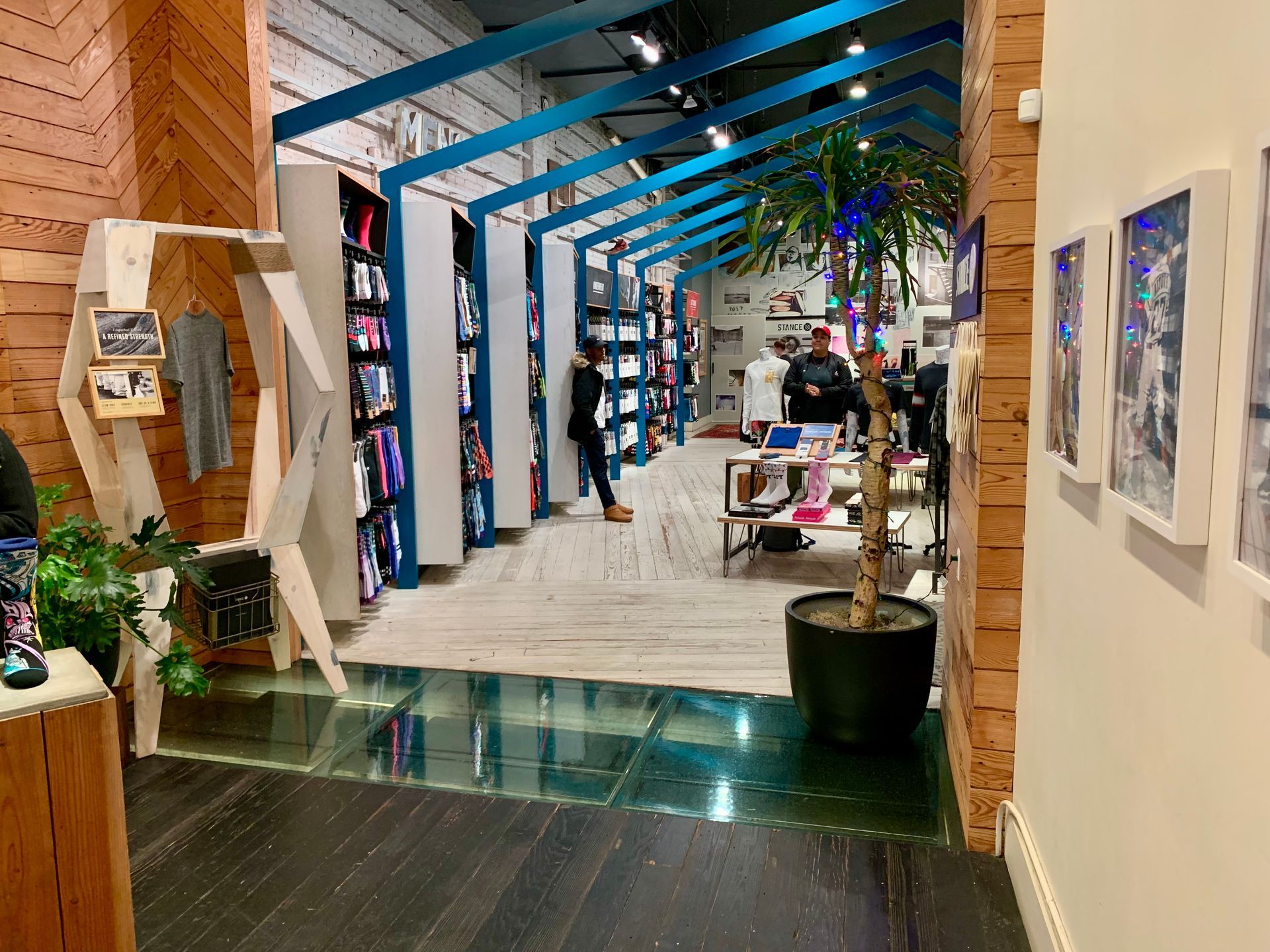 Shoe store interior with blue shelving, wooden accents, glass floor, and customers browsing.