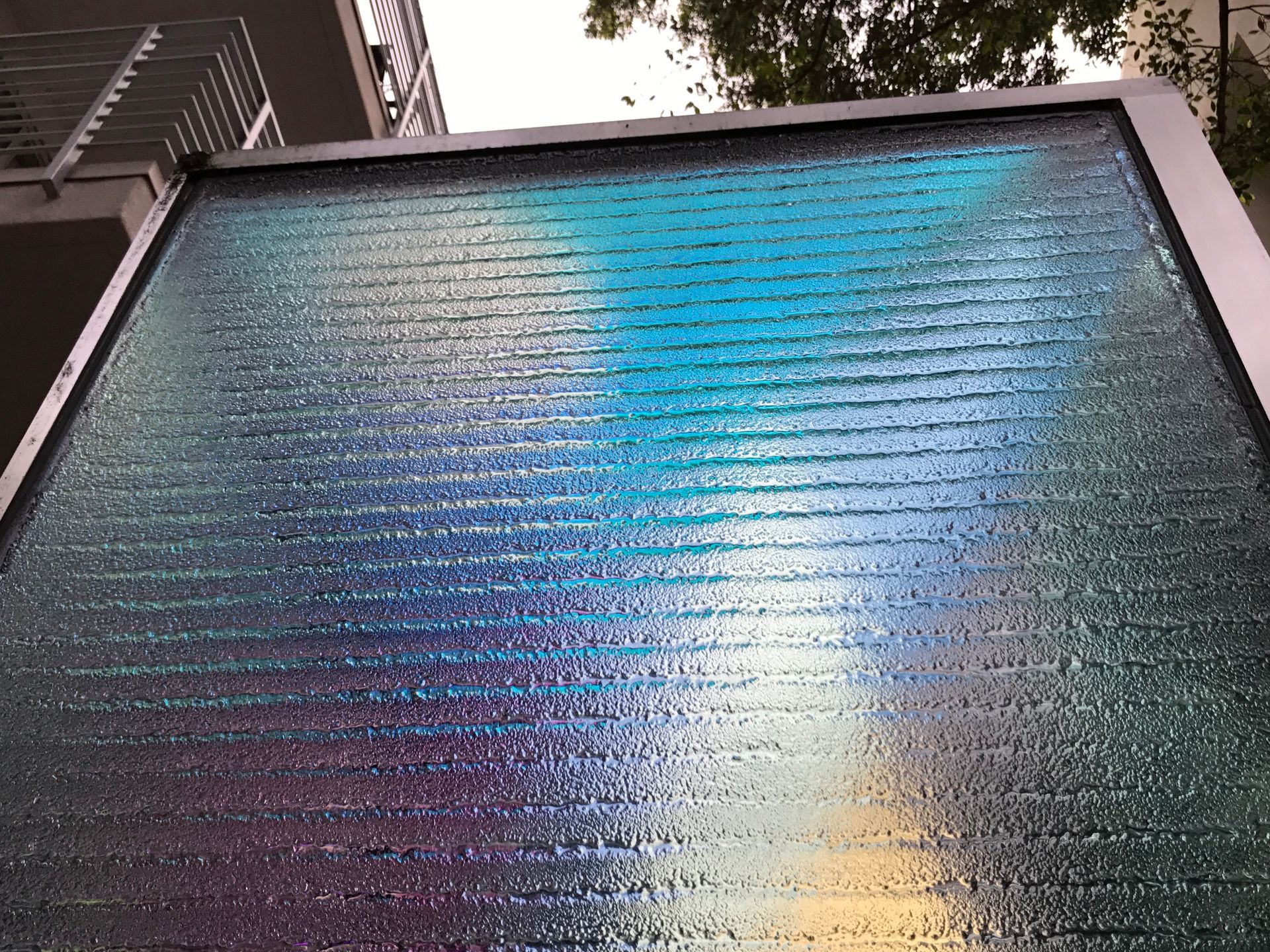 A vertical, textured glass feature illuminated with shimmering blue, teal, and purple light, viewed from below.