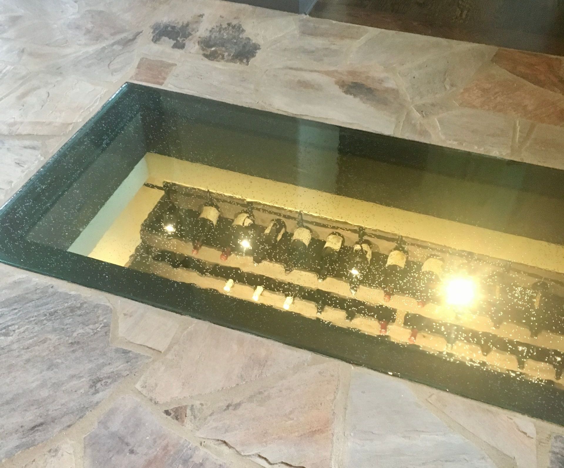 A glass floor display case filled with bottles of wine