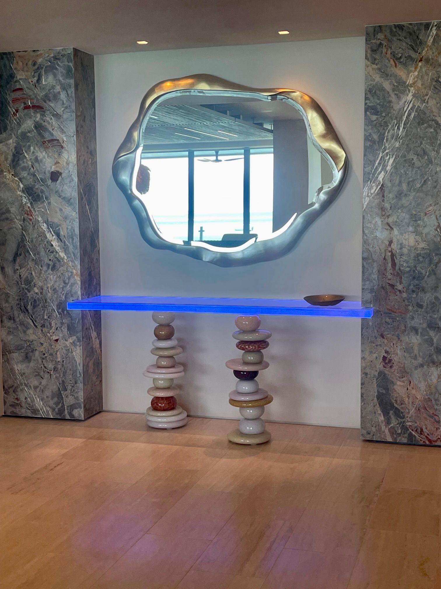 Silver-framed organic-shaped mirror above a stacked ceramic console table. The console has a blue glass top.