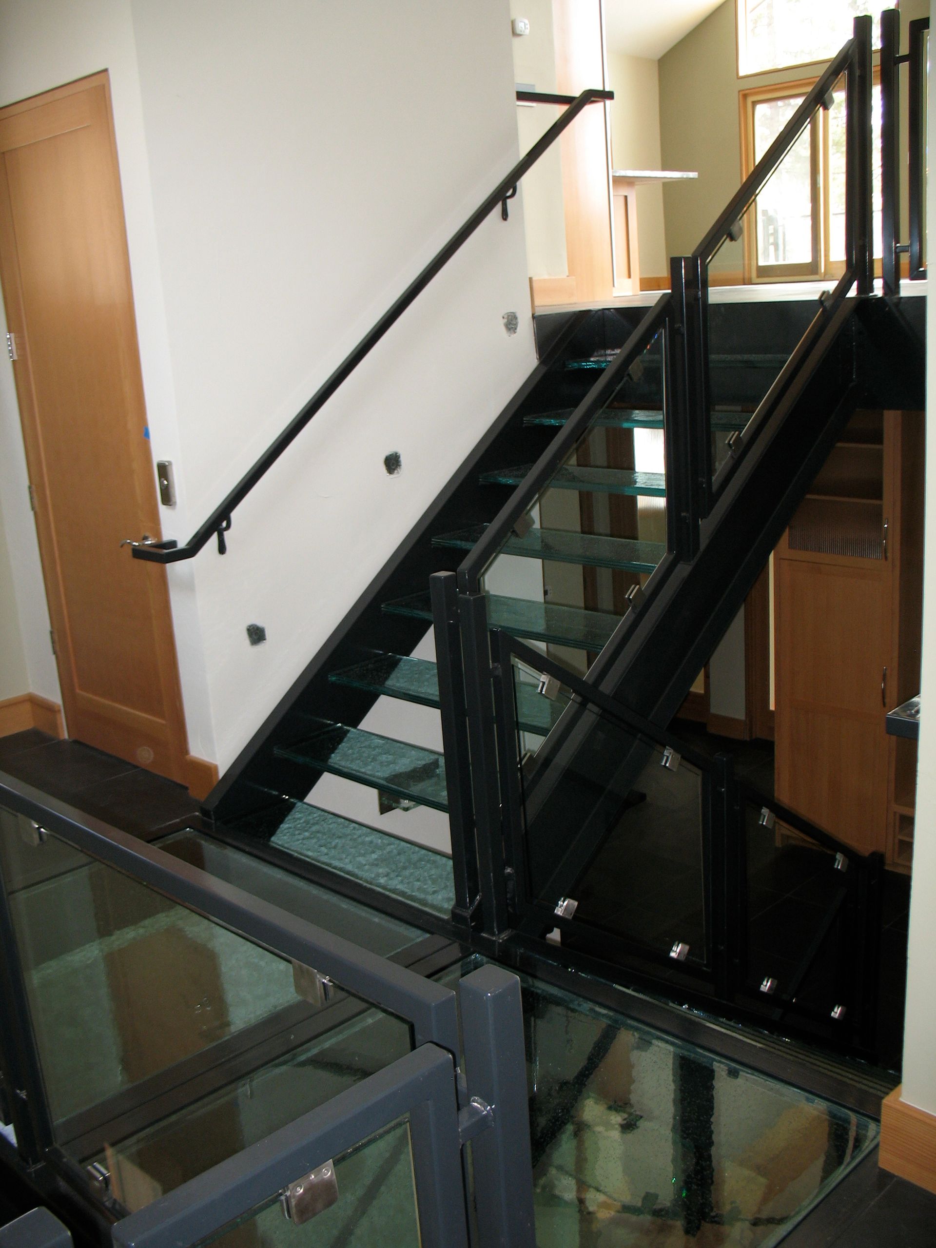 Black metal staircase with glass steps and handrails, set in a modern home.