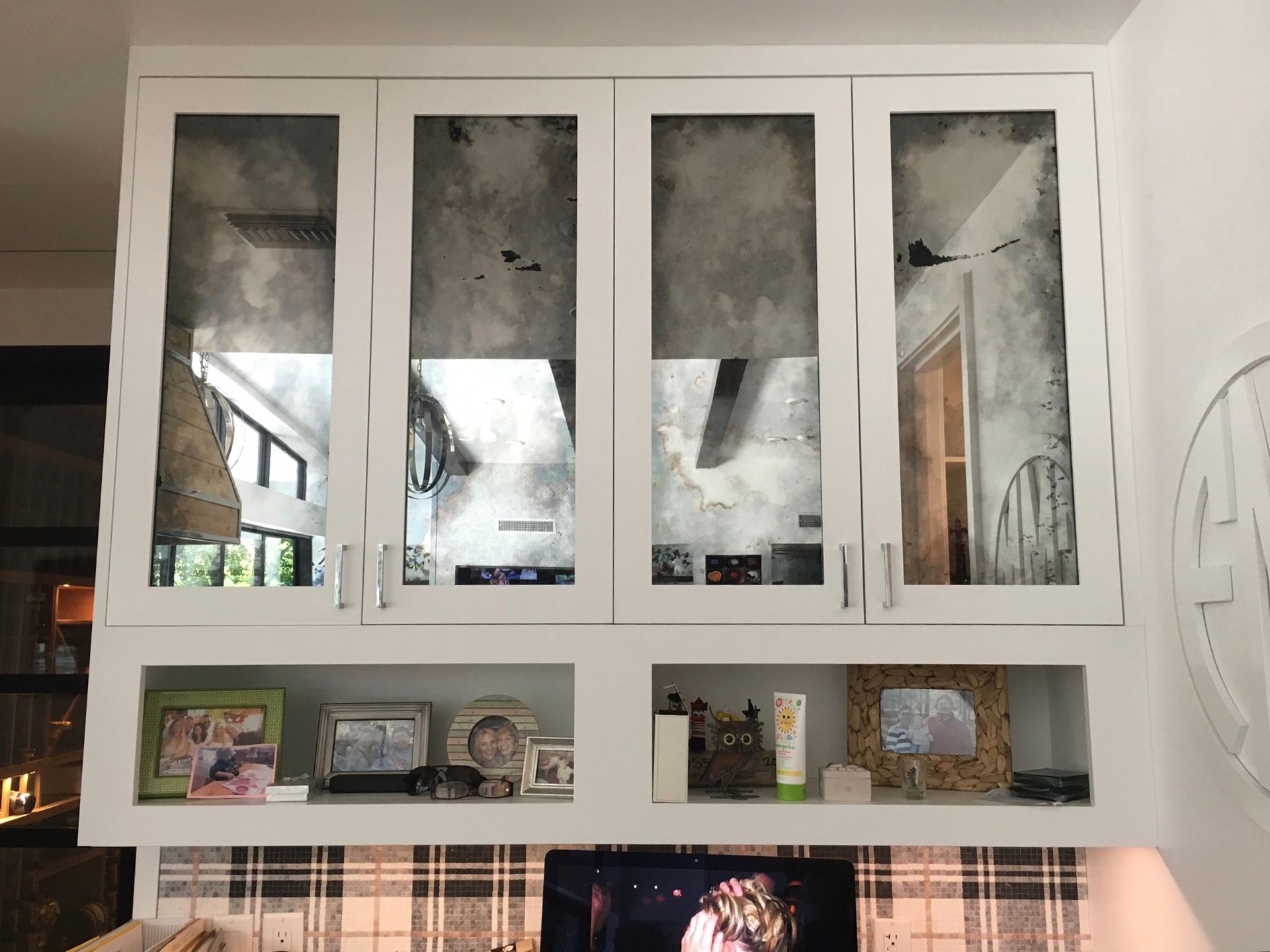 White cabinet with antique mirror doors above display shelf holding photos and toiletries.