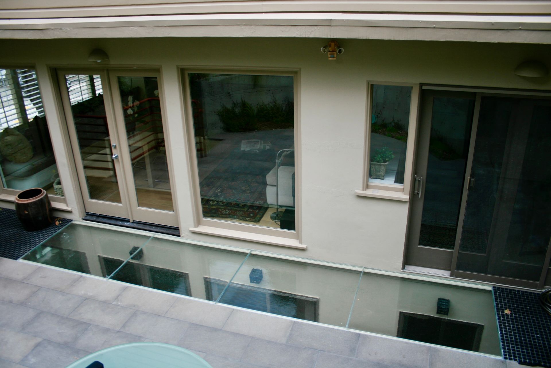 A modern house exterior featuring a glass floor section on a patio, overlooking a lower level and glass doors.