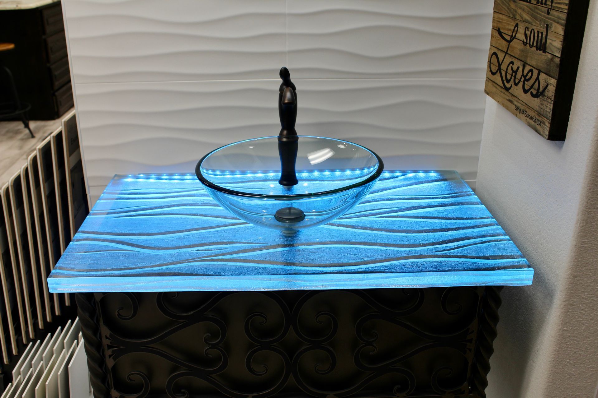 A bathroom sink with a blue glass counter top and a sign on the wall.