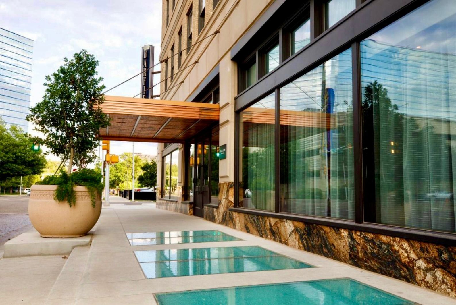 Exterior of a building with a sidewalk and large windows, reflecting a sky. Glass flooring panels in the side walk. 