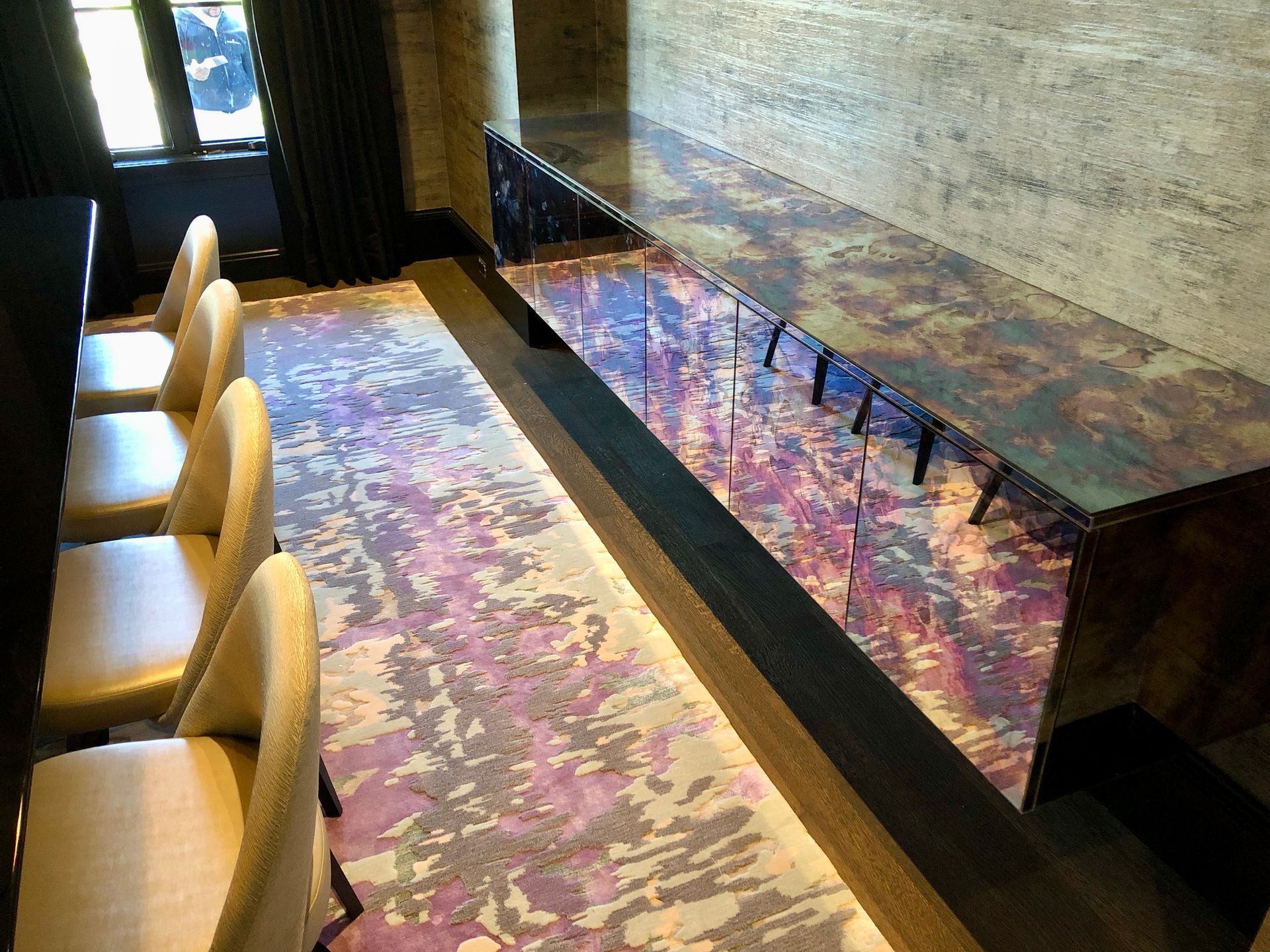 A dining room with a long table and chairs and a purple rug.