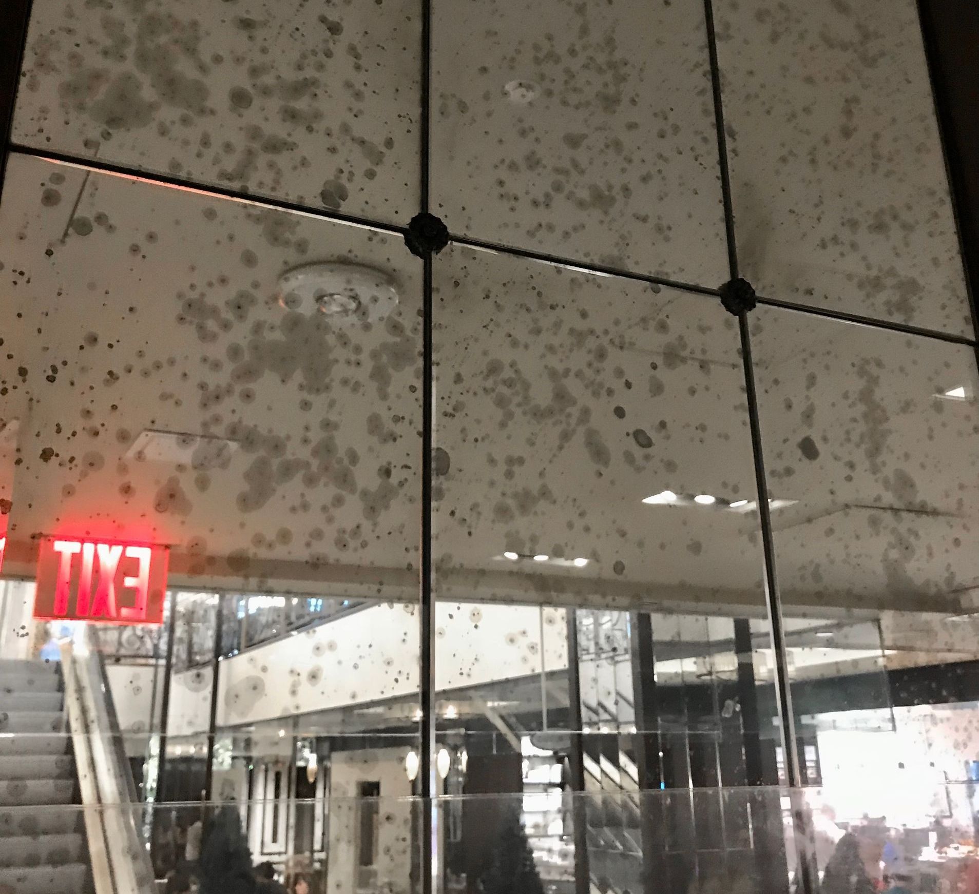 A red exit sign hangs above an escalator in a building