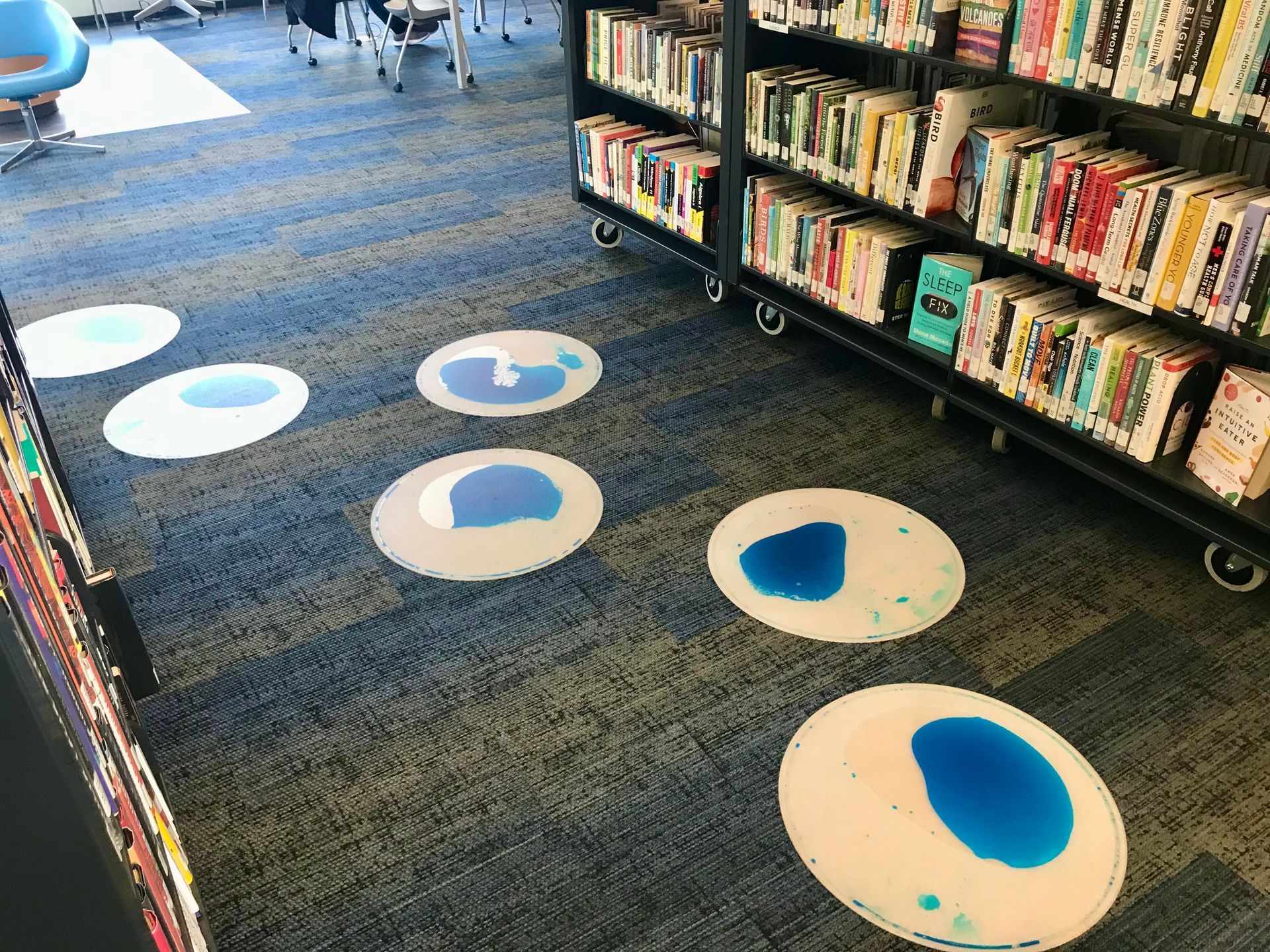 Library floor with blue and white puddle-shaped liquid filled tiles, near a bookshelf.
