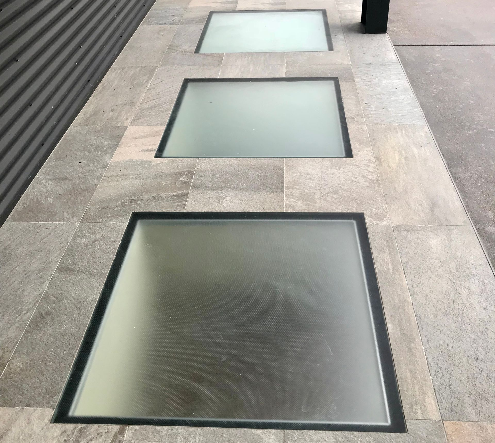 Three square, translucent glass panels embedded flush into a stone walkway, viewed at an angle.