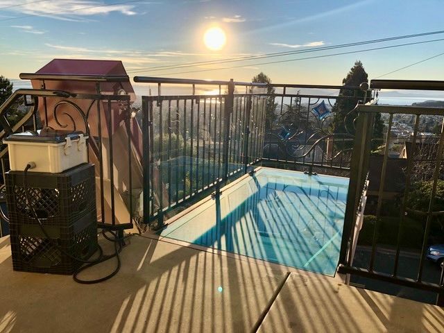 A pool covered in blue plastic on a deck overlooking a sunset landscape, with a small tank resting on a black crate.