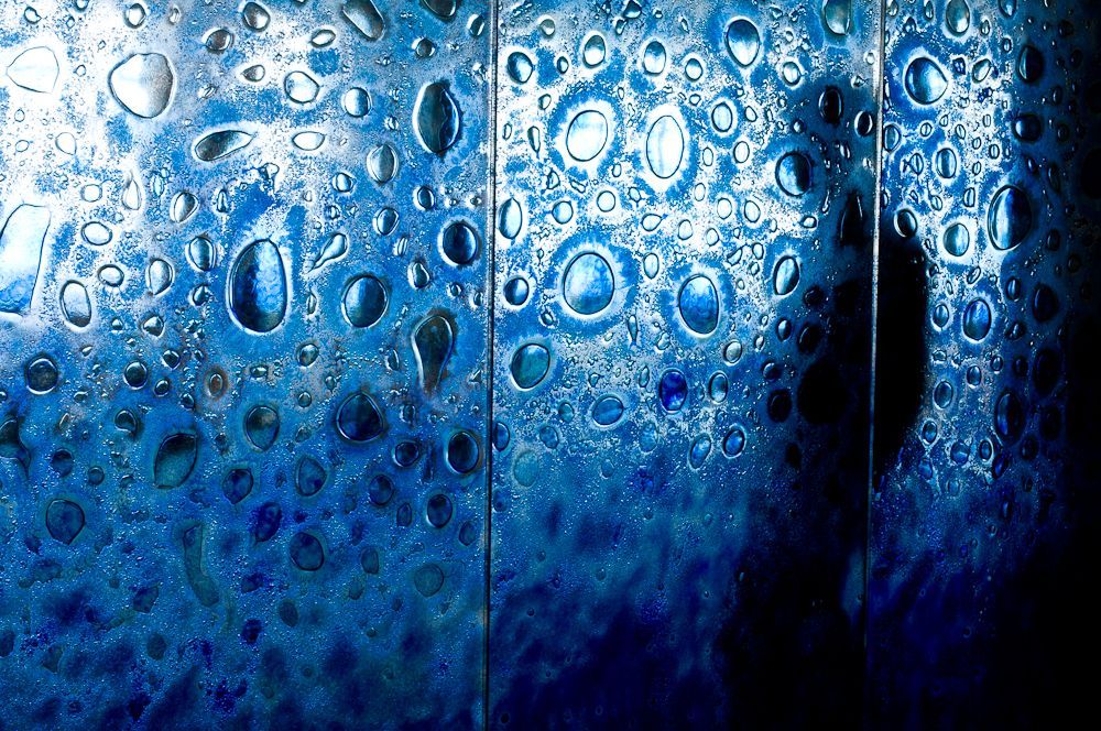 A person is standing in front of a blue decorative glass wall 