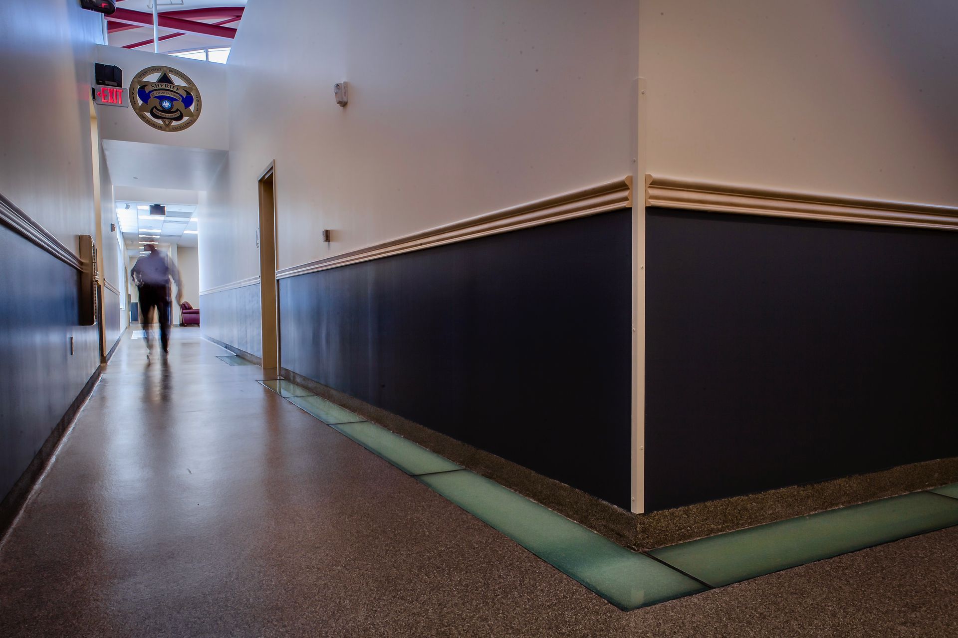 Hallway with dark blue wainscoting, light floor, and a person walking towards the end.
