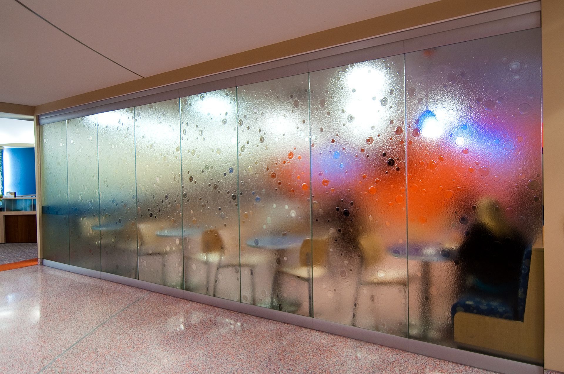 A restaurant interior viewed through a textured glass partition with a decorative, textured water-droplet pattern.