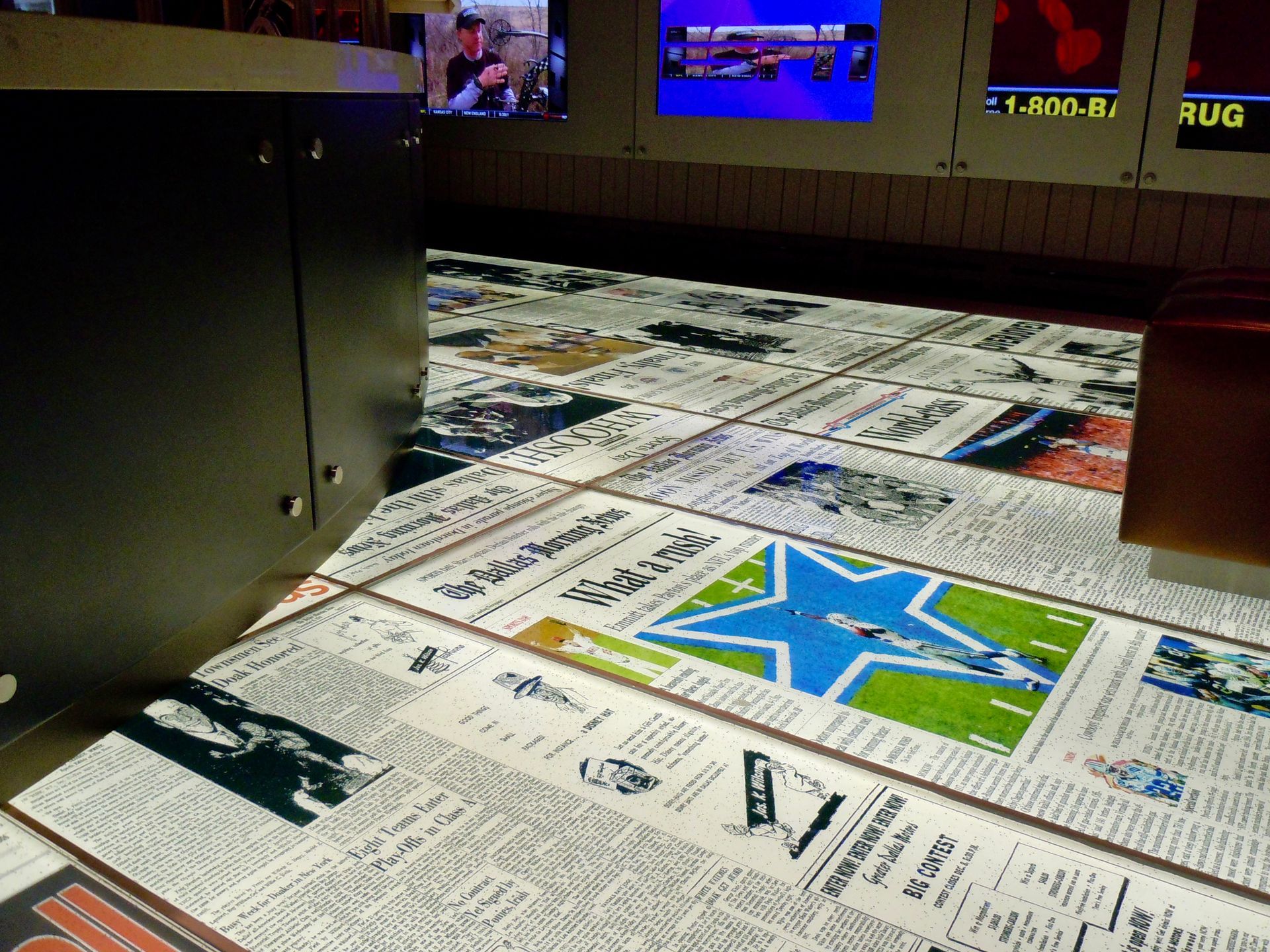Glass Floor with newspaper-themed tiles; TV screens on the wall above.