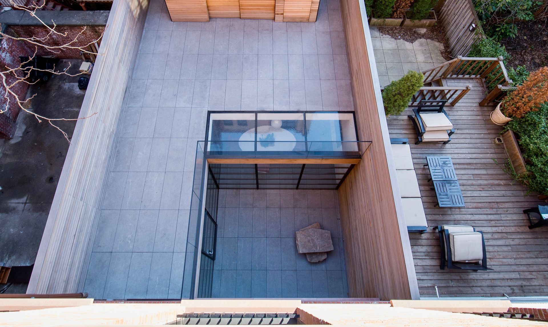 High-angle view of a split-level outdoor space with gray stone patio areas, a glass-roofed section, and wooden decking.