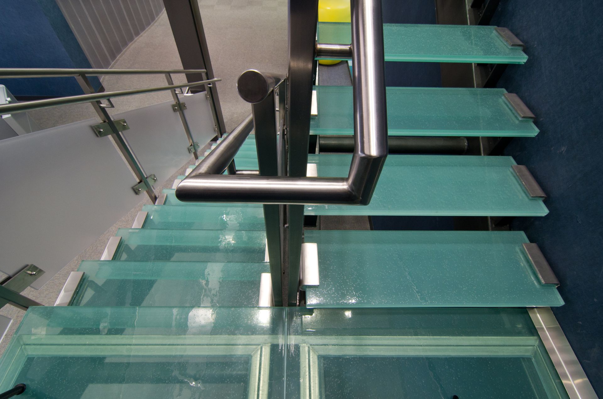 Glass staircase with stainless steel railings and turquoise steps.