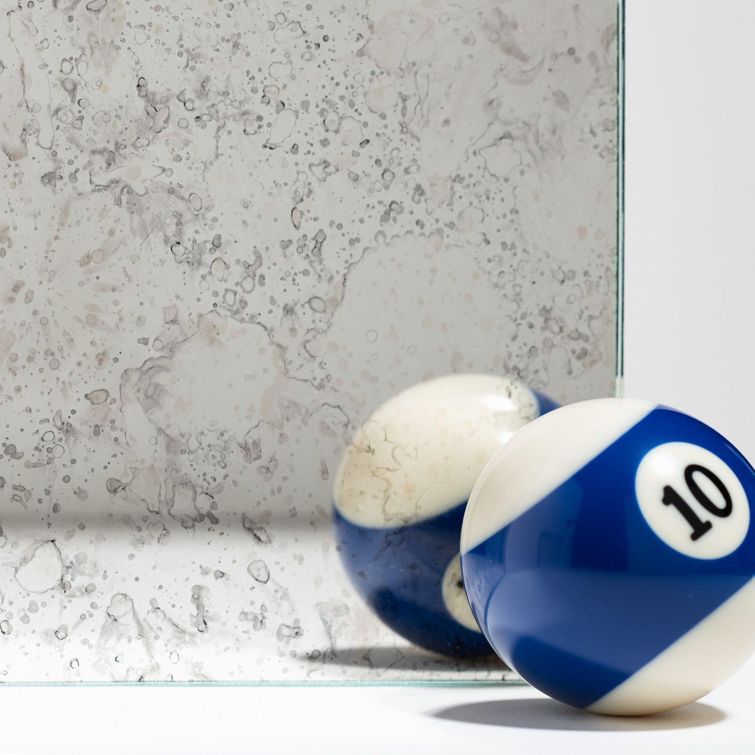 A number 10 billiard ball sits in front of a piece of antiqued, distressed-looking mirror glass.