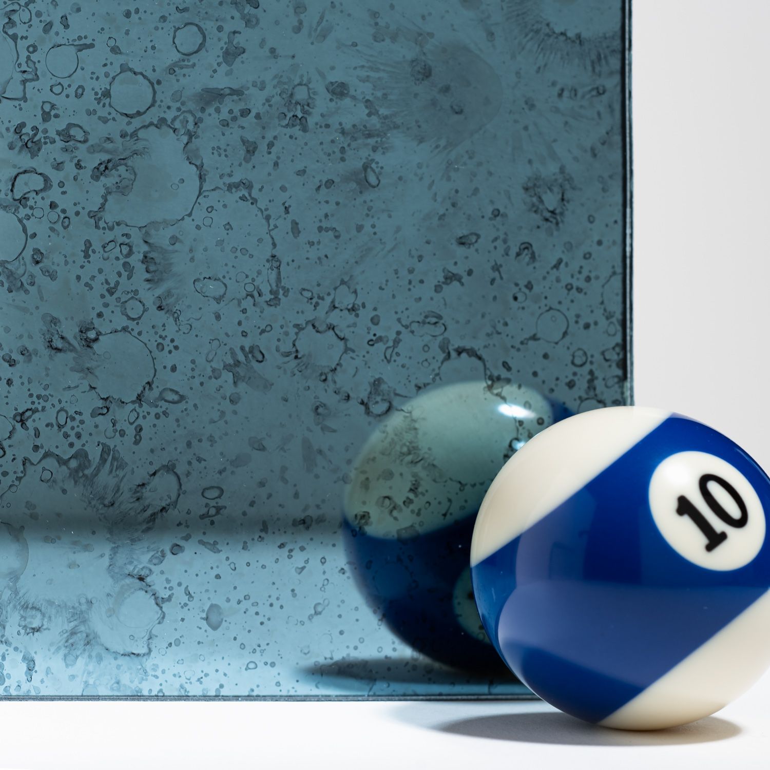 A number 10 pool ball resting in front of its reflection on a distressed, blue-tinted antique mirror.