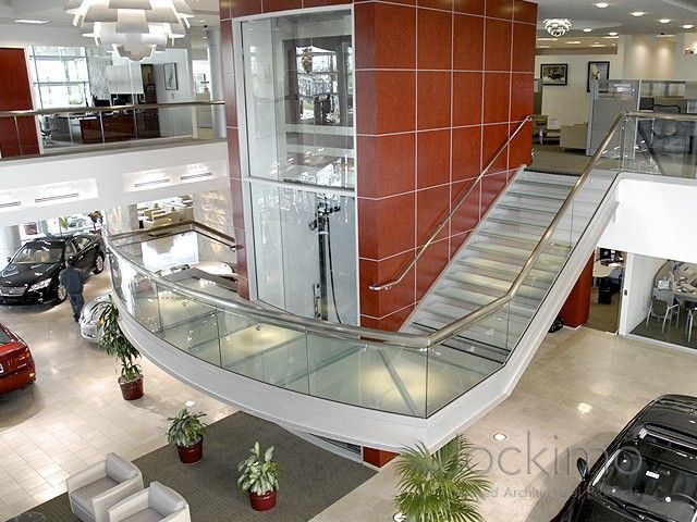 Modern car dealership interior with curved glass walkways, red accents, and multi-level design.