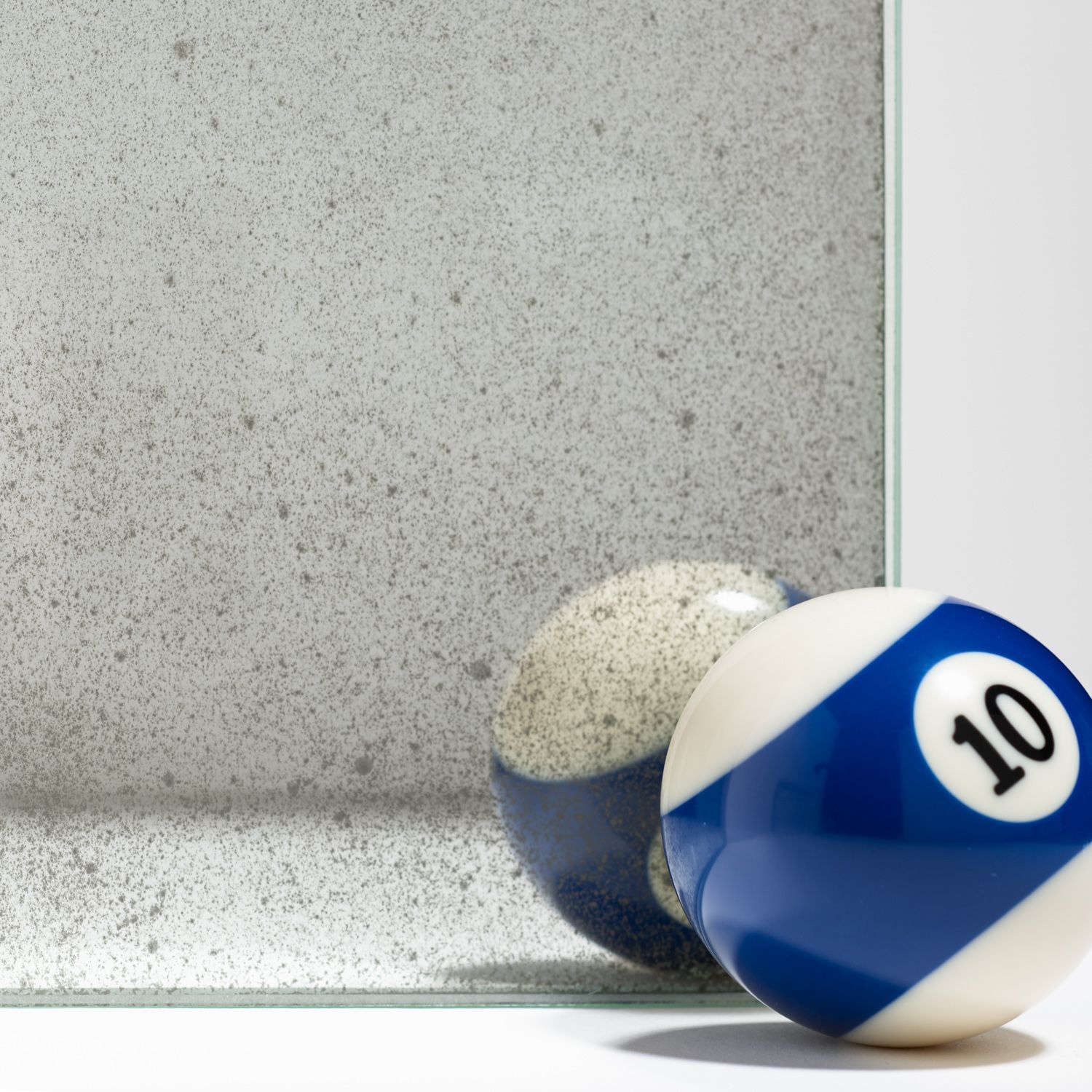 A blue and white number 10 billiard ball rests against a textured, light gray mirror surface, showing its reflection.