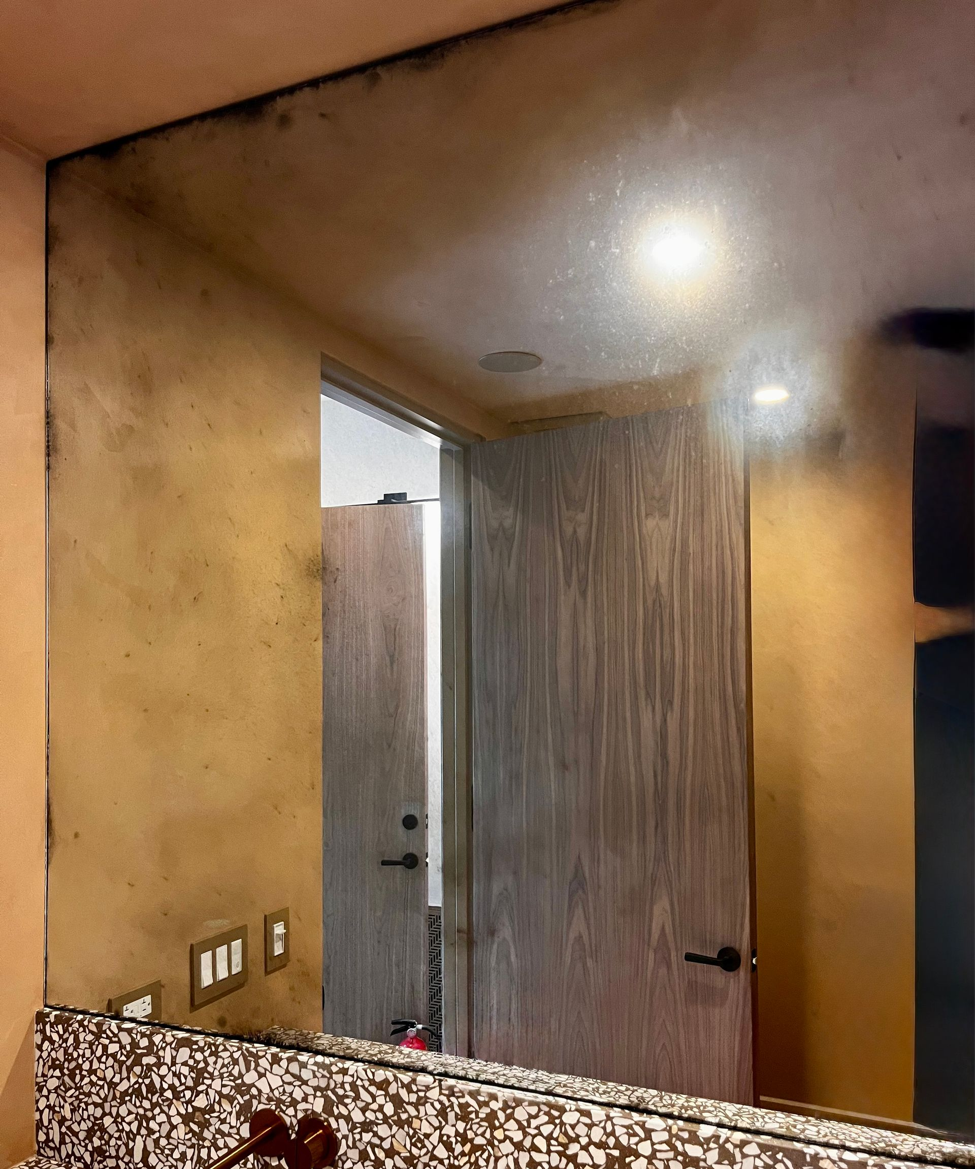 A wall mirror with significant dark, blotchy oxidation along its top and left edges, mounted above a speckled countertop.