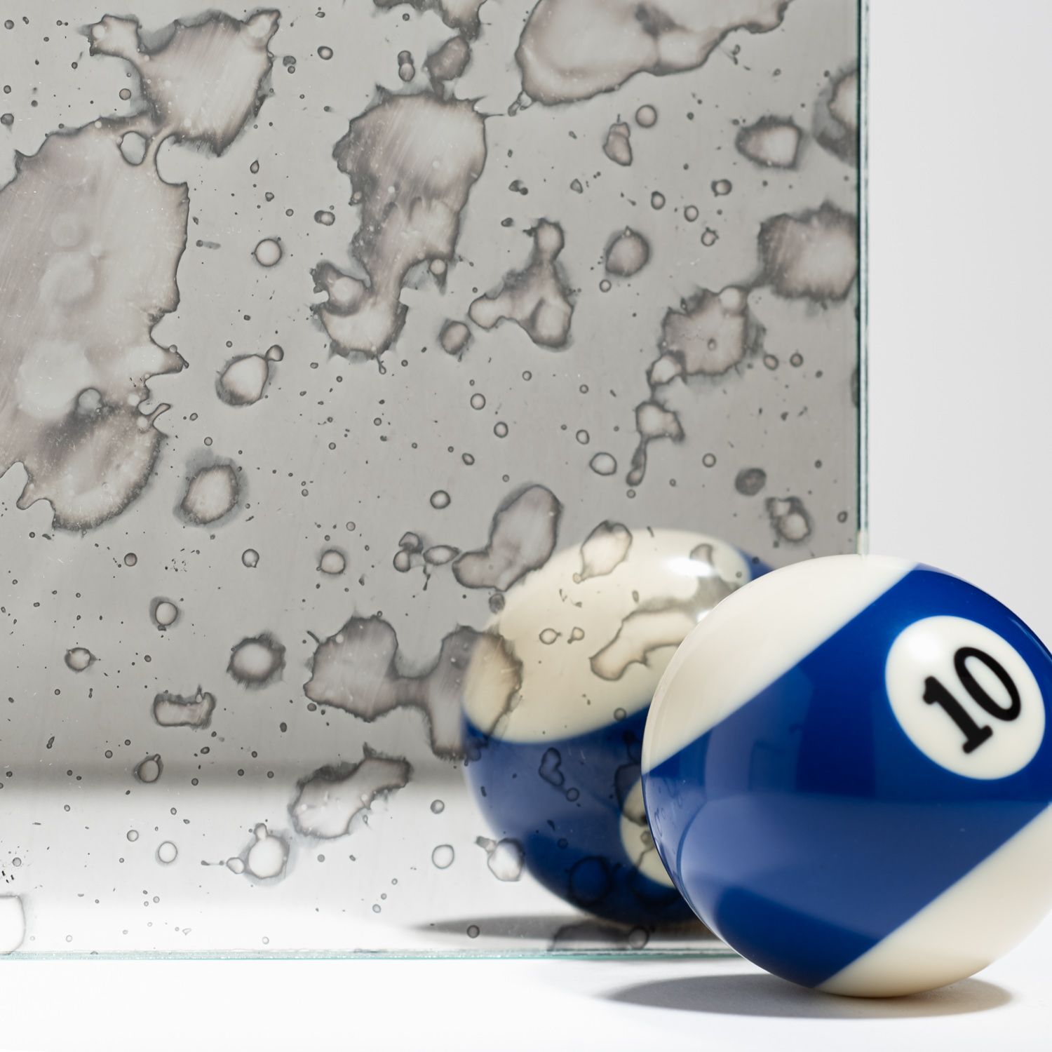 A blue and white number 10 billiard ball sits in front of a piece of distressed, antiqued mirror glass.