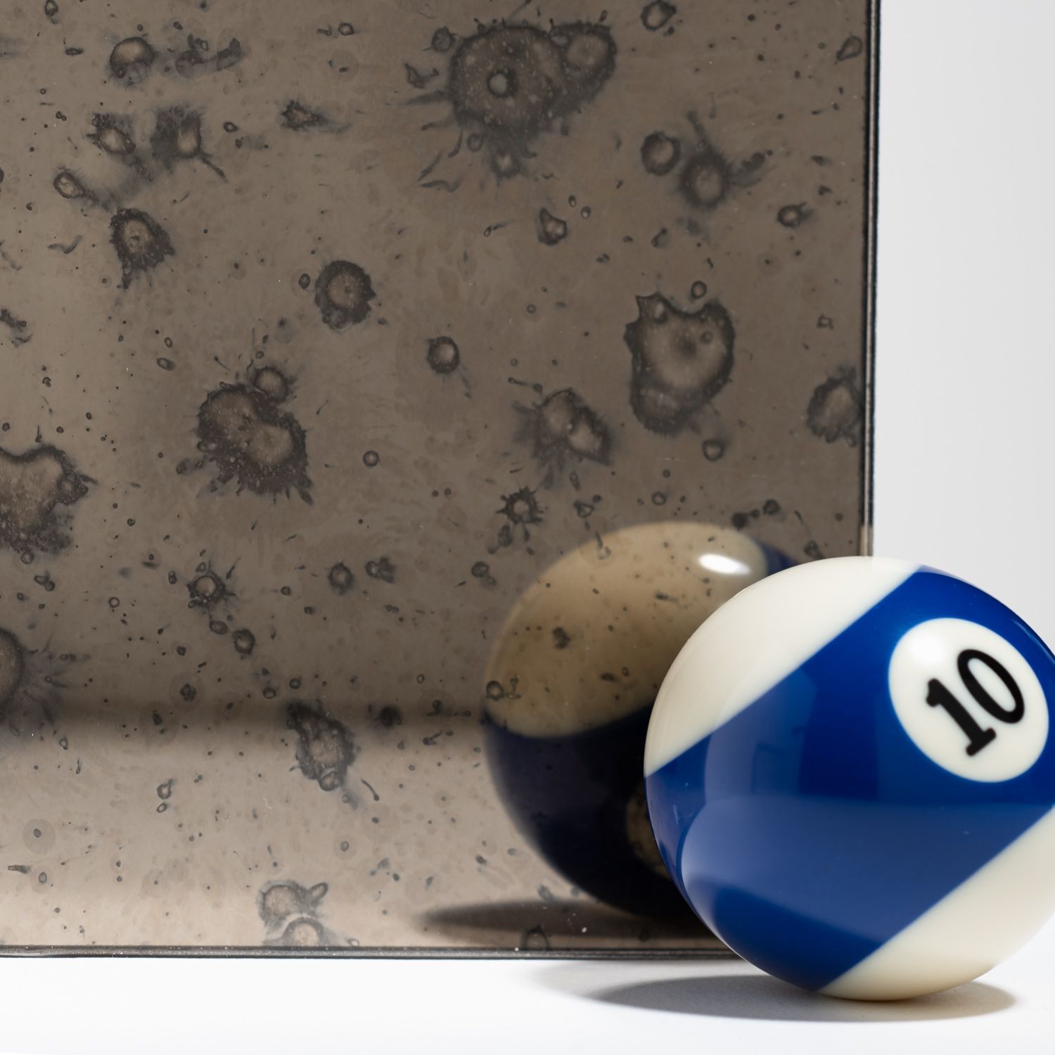 A blue and white number 10 billiard ball sits next to its reflection in a distressed, antique-style mirror.