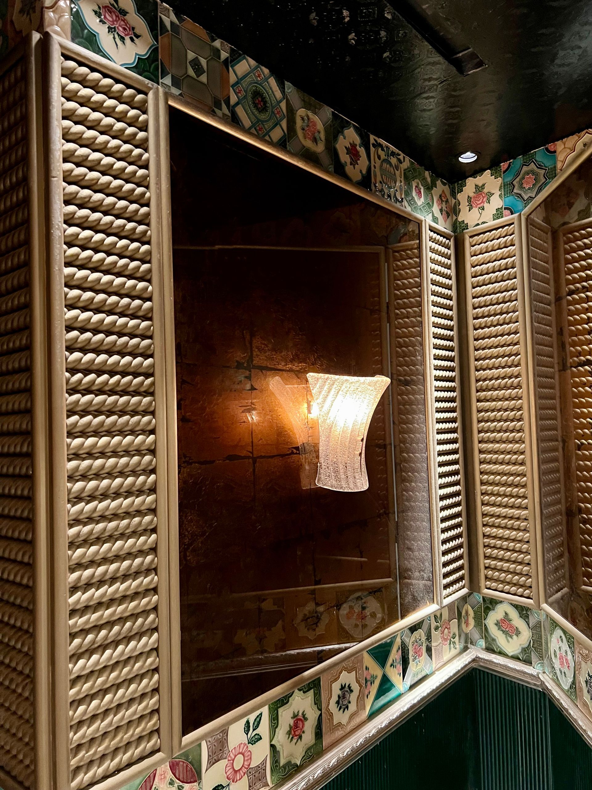 An interior view of an antique mirrored alcove framed by rope-textured molding and decorative tiles.