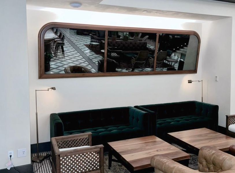 A lounge area with dark green sofas, wooden tables, and a large mirror reflecting the room.