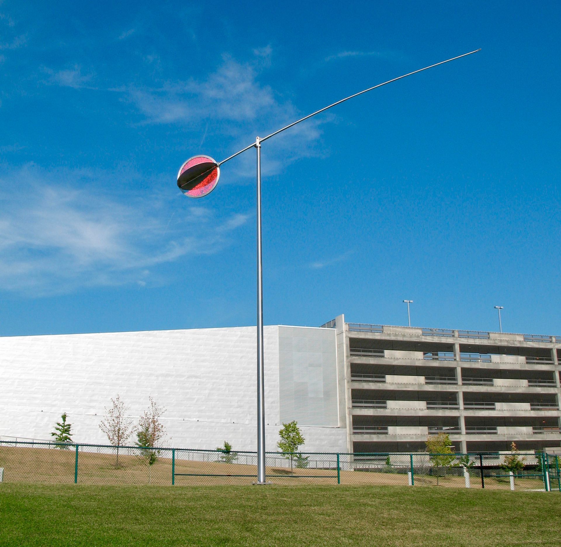 Modern outdoor sculpture; a tall metal pole with a circular disc and long, thin arm against a blue sky.