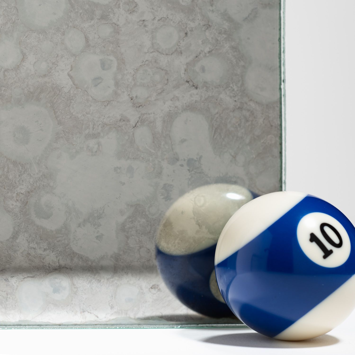 A number 10 billiard ball sits in front of a piece of antique, mottled mirror glass, showing a reflection of the ball.