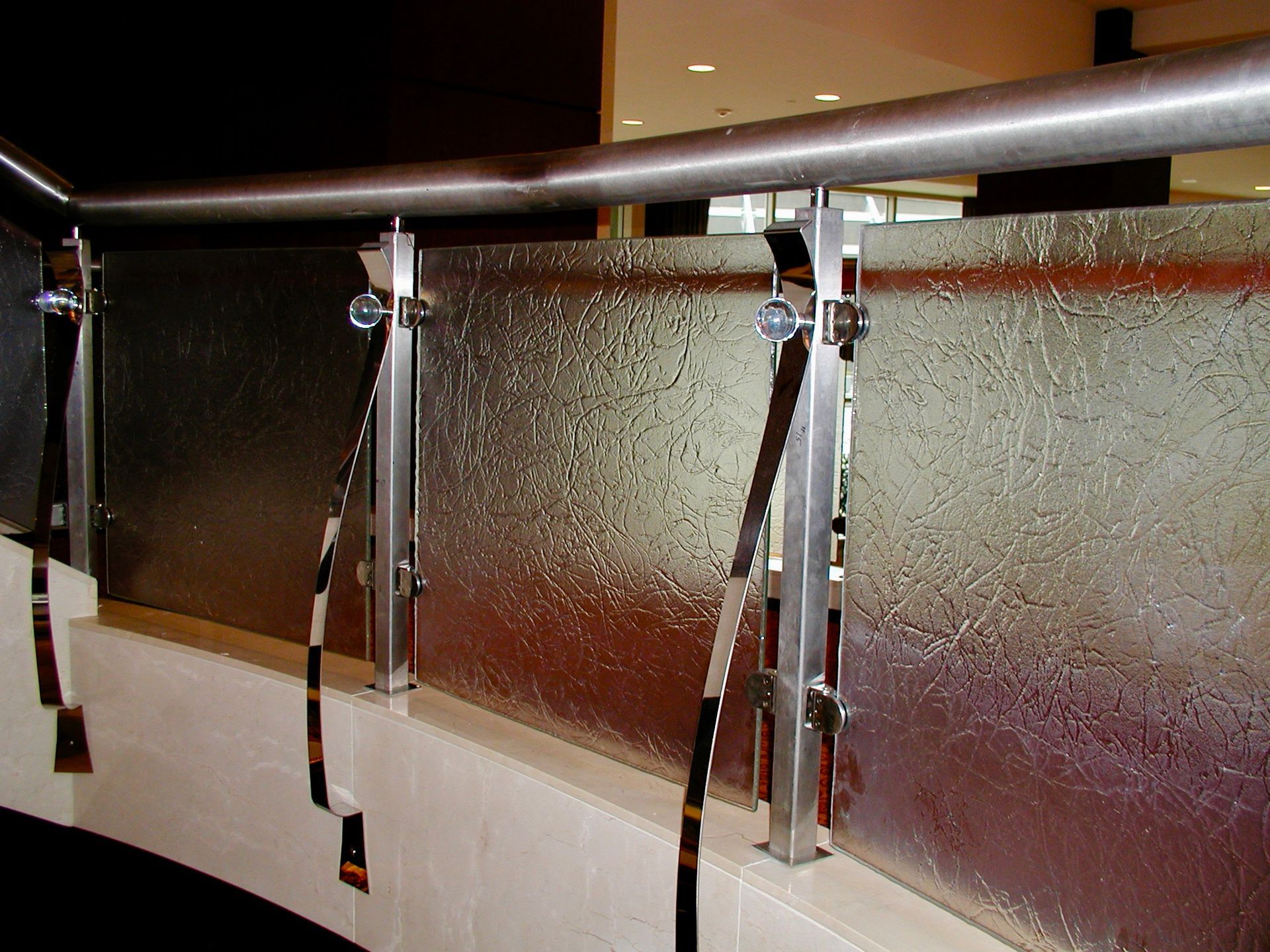Glass railing with stainless steel supports and textured glass, in a building interior.