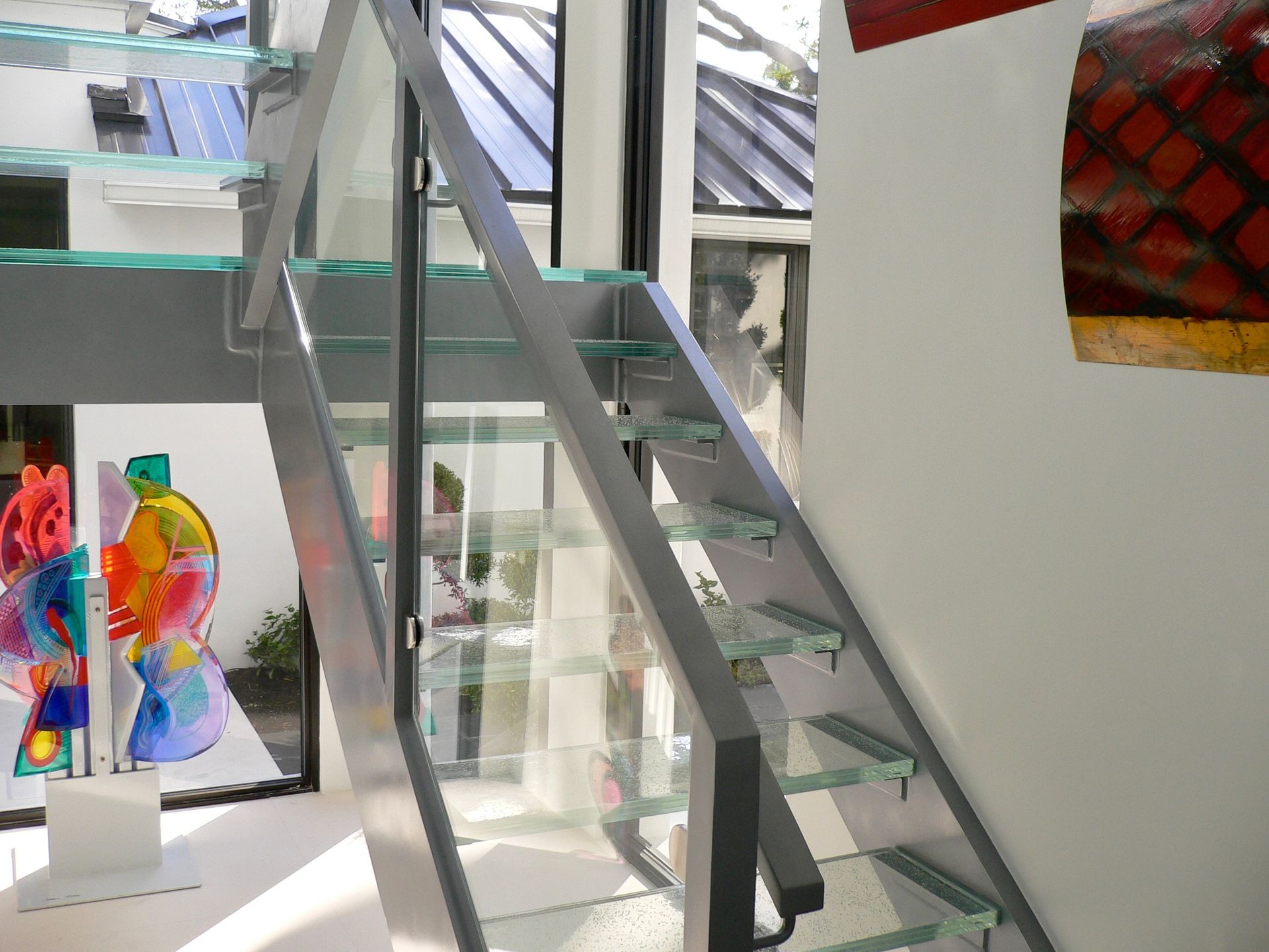 A modern staircase with clear glass treads and grey metal supports, situated in a brightly lit, gallery-like interior.