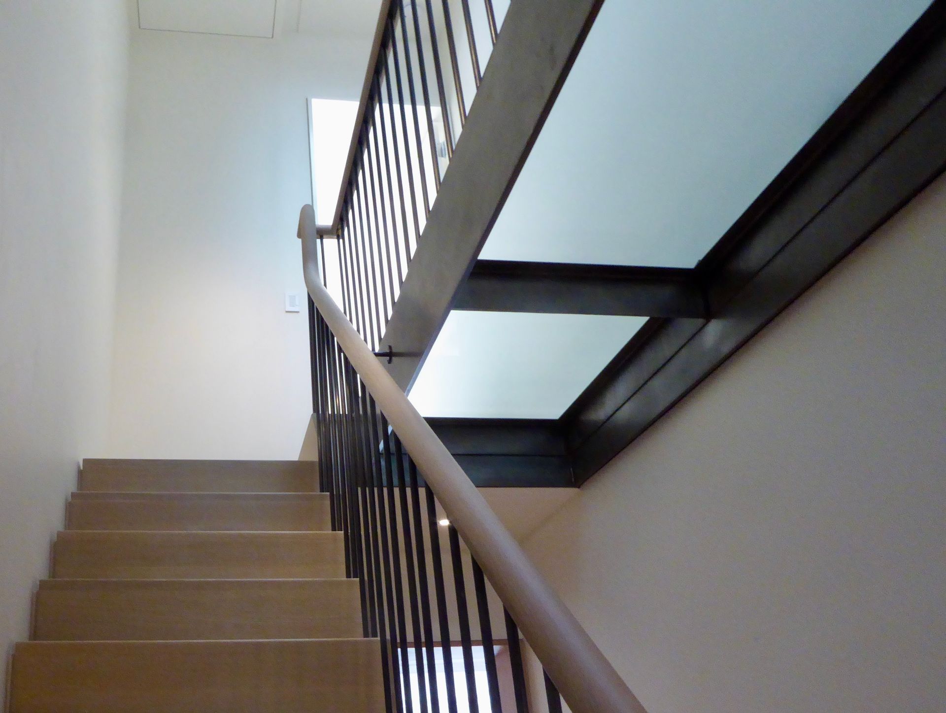 Staircase with light-colored steps and a modern railing featuring black metal supports and a handrail.