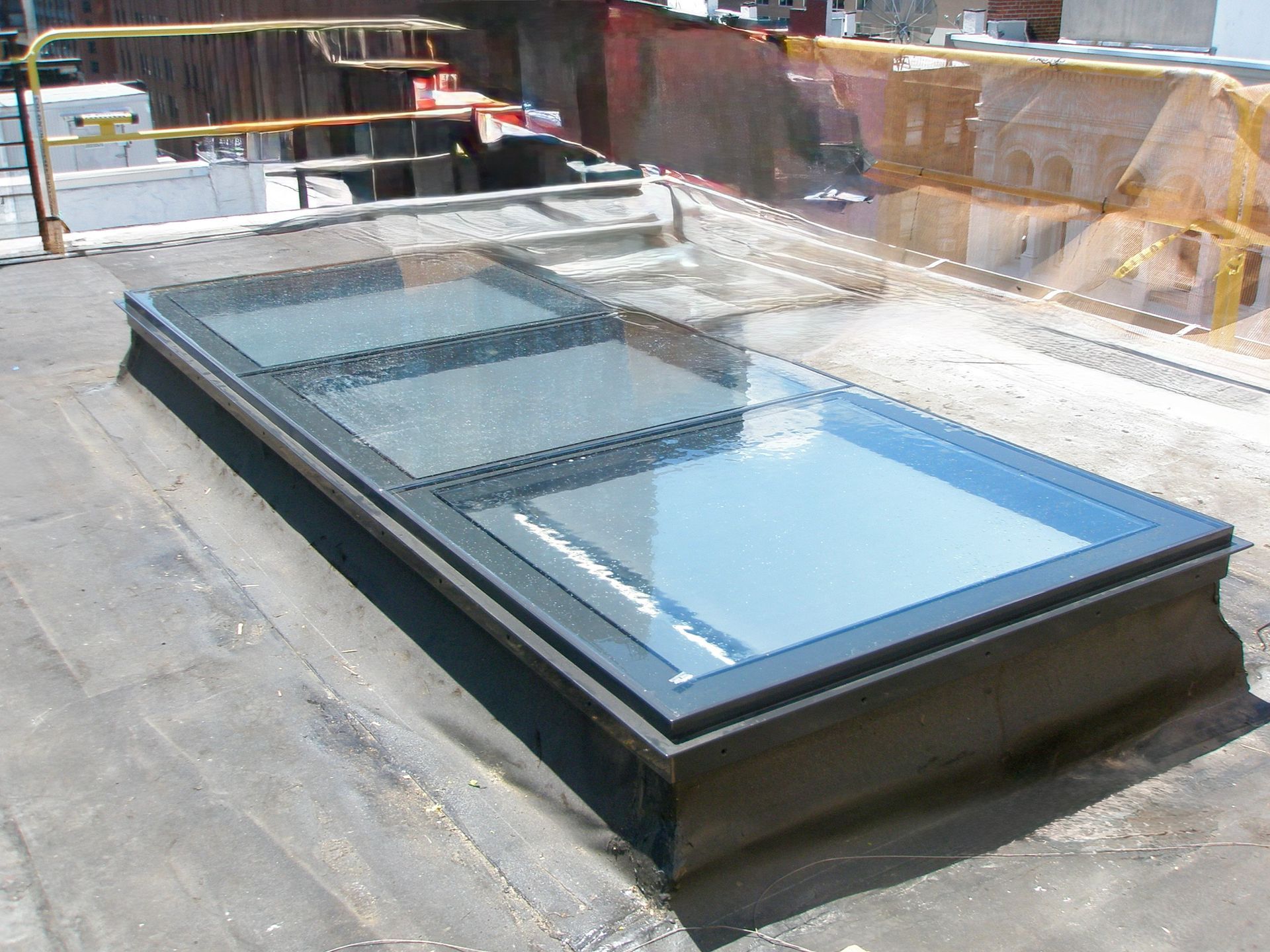 A rectangular glass skylight installed on a dark flat roof during construction.