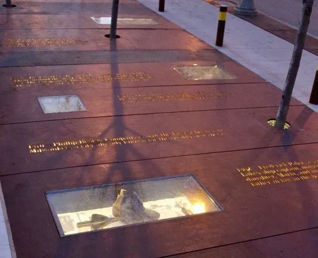 Red pavement with recessed glass display windows containing historic artifacts and gold inscriptions on a sidewalk.