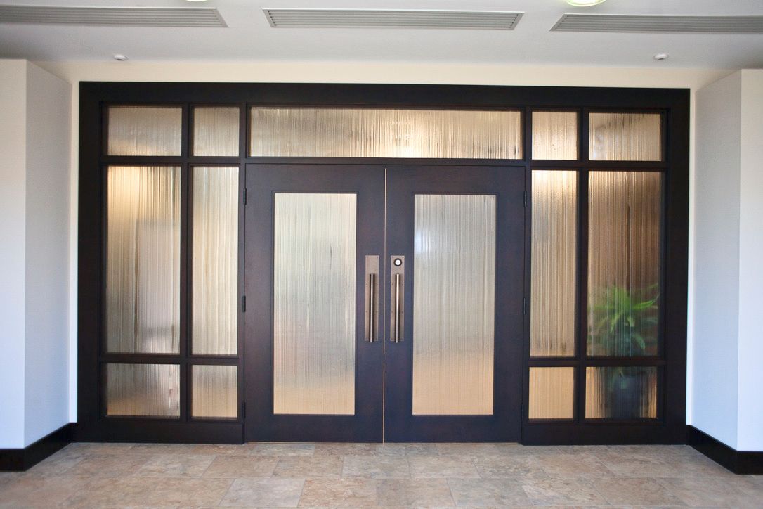 Double doors with textured reeded glass panels, black frame, and bronze handles in a neutral-colored foyer.