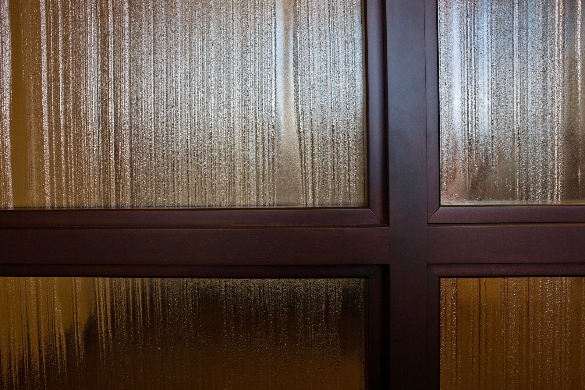A close-up view of textured, vertical-striped glass panes set within a dark brown wooden grid frame.