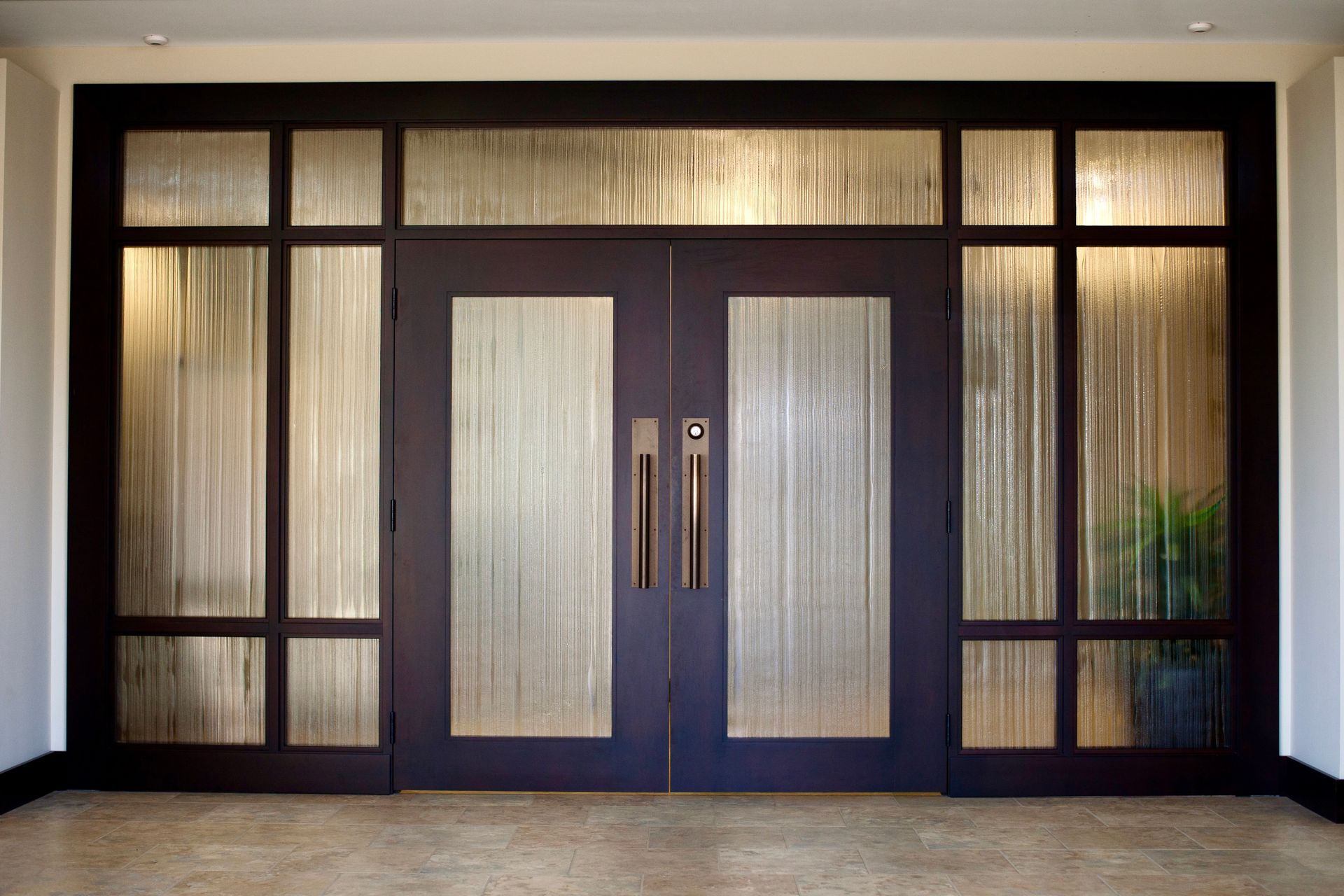 A dark-framed double entryway door with vertical, textured glass panels, set in a neutral-toned foyer.