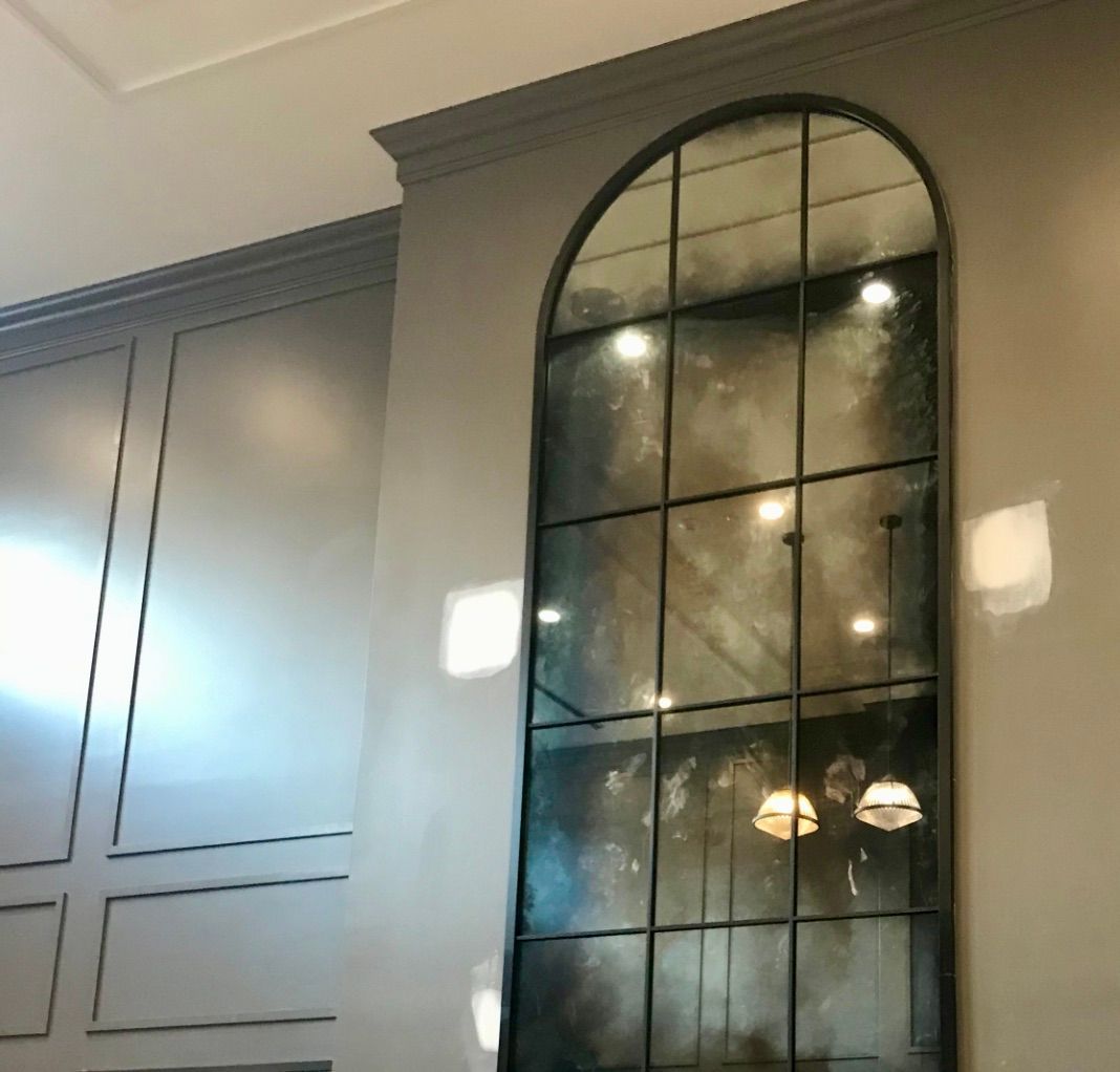 An arched, grid-paned antique mirror mounted on a gray paneled wall.